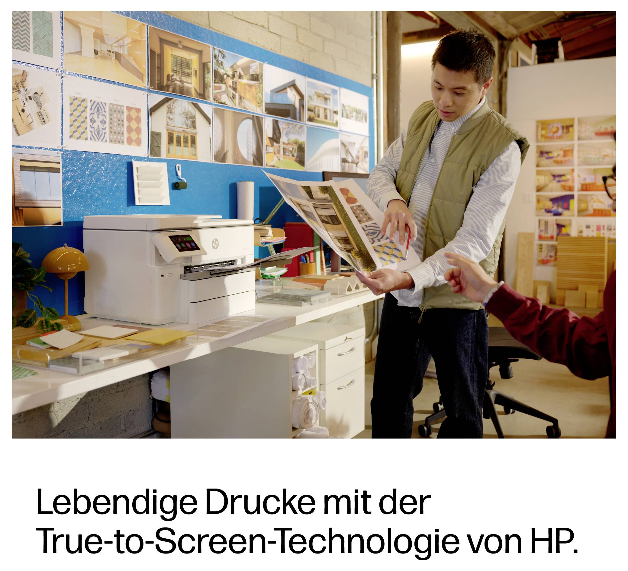 Mann untersucht Druckprobe in einem Designstudio; deutscher Anzeigentext lautet „Lebendige Drucke mit der True-to-Screen-Technologie von HP."