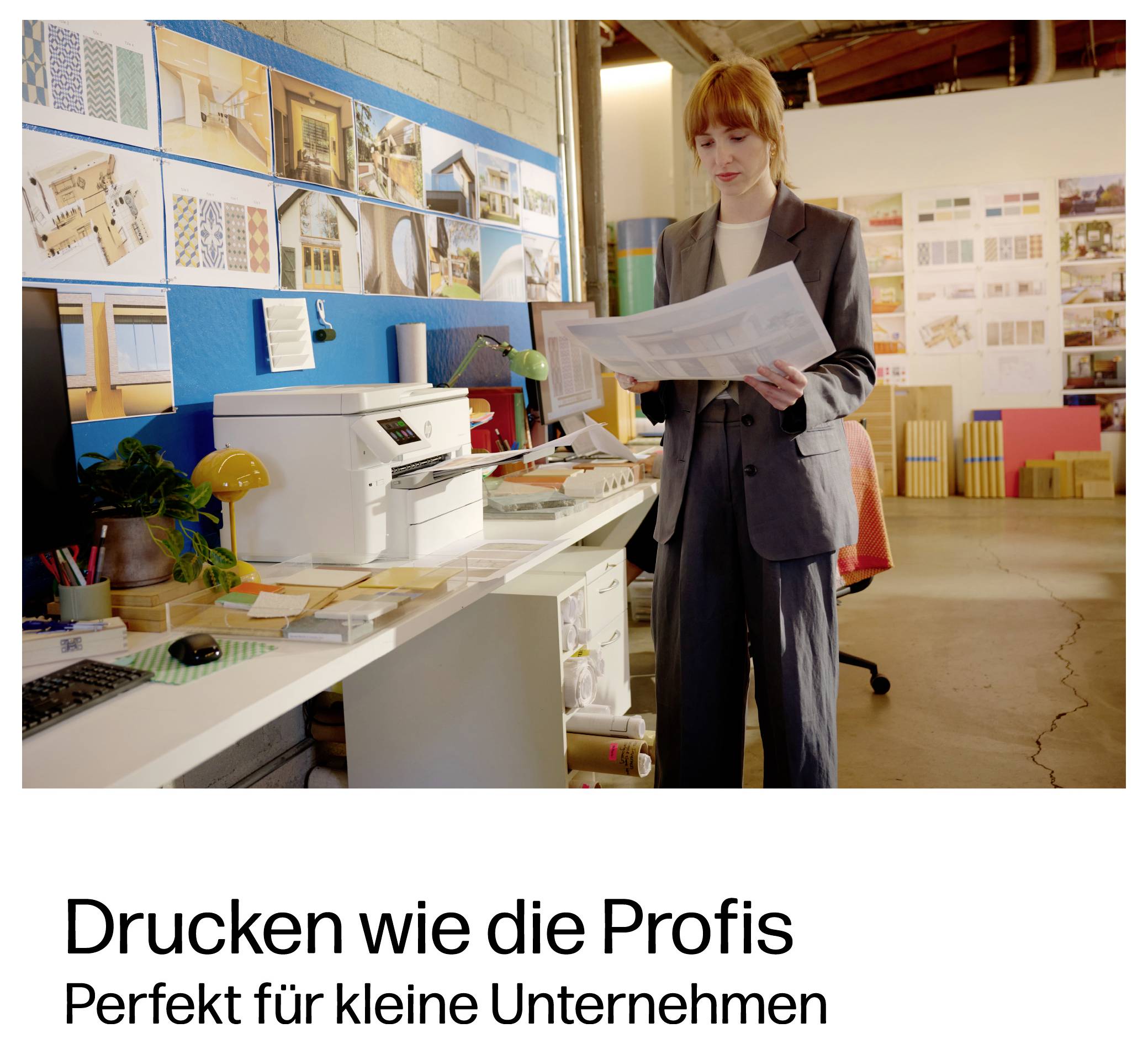 Frau überprüft einen großen Ausdruck in einem kreativen Büro mit einem Desktop-Drucker; der Text lautet „Drucken wie die Profis" und „Perfekt für kleine Unternehmen".
