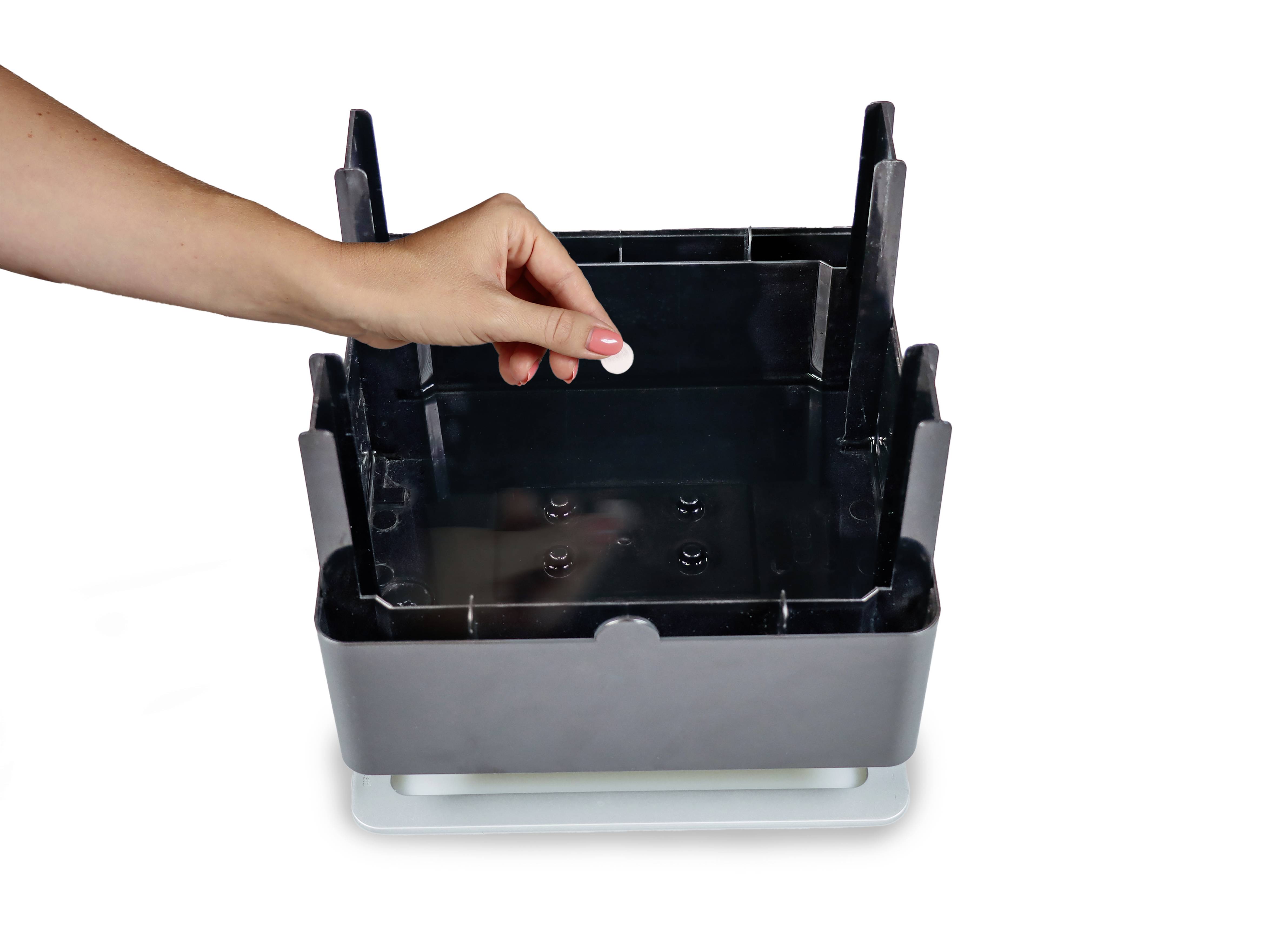 Eine Hand hält eine kleine Trennwand, die in einen schwarzen Behälter mit offenen Seiten gesteckt wird.