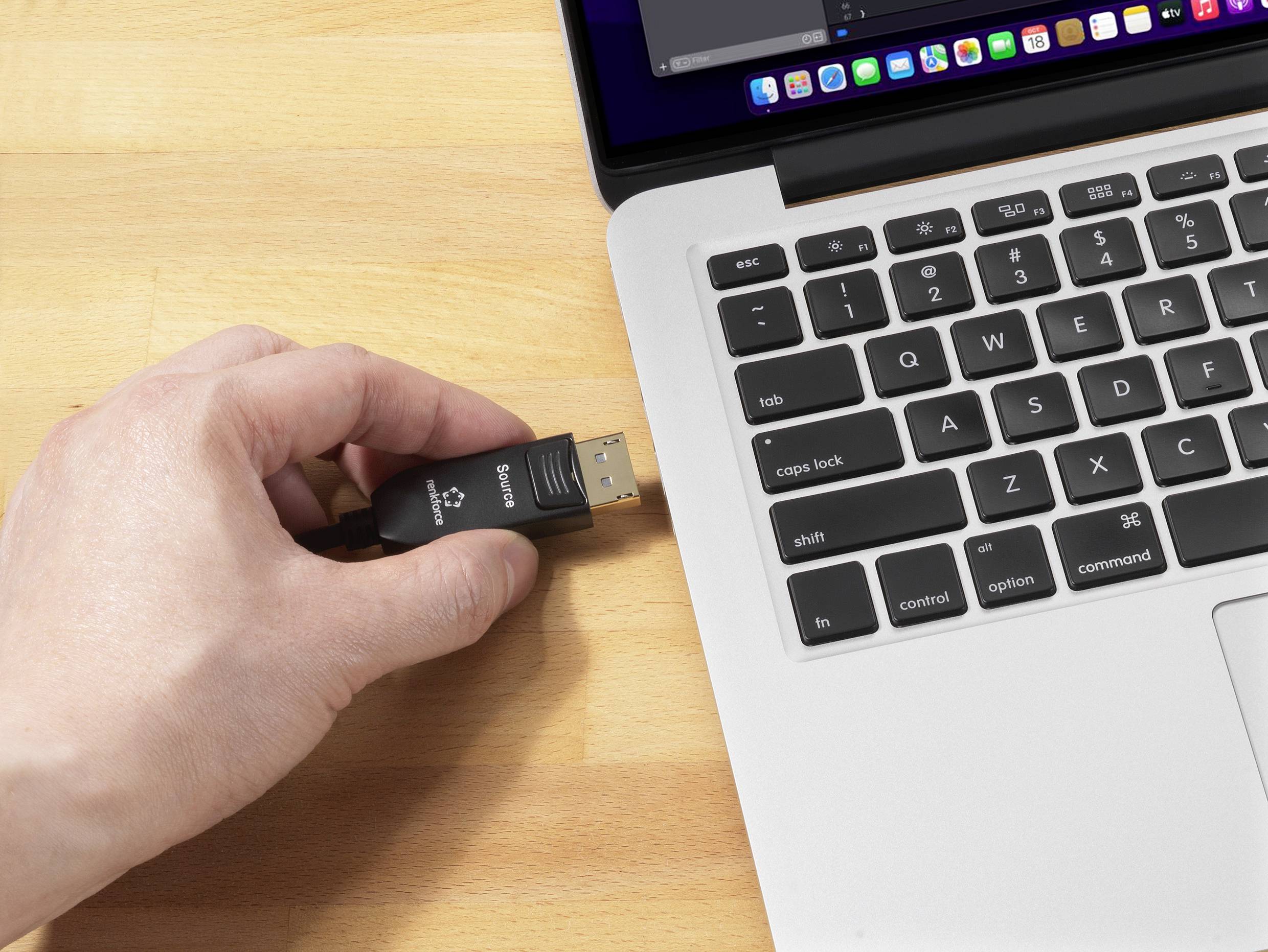 Eine Hand steckt einen USB-Stick in einen Laptop auf einem Holztisch. Der Bildschirm des Laptops zeigt teilweise geöffnete Programme.