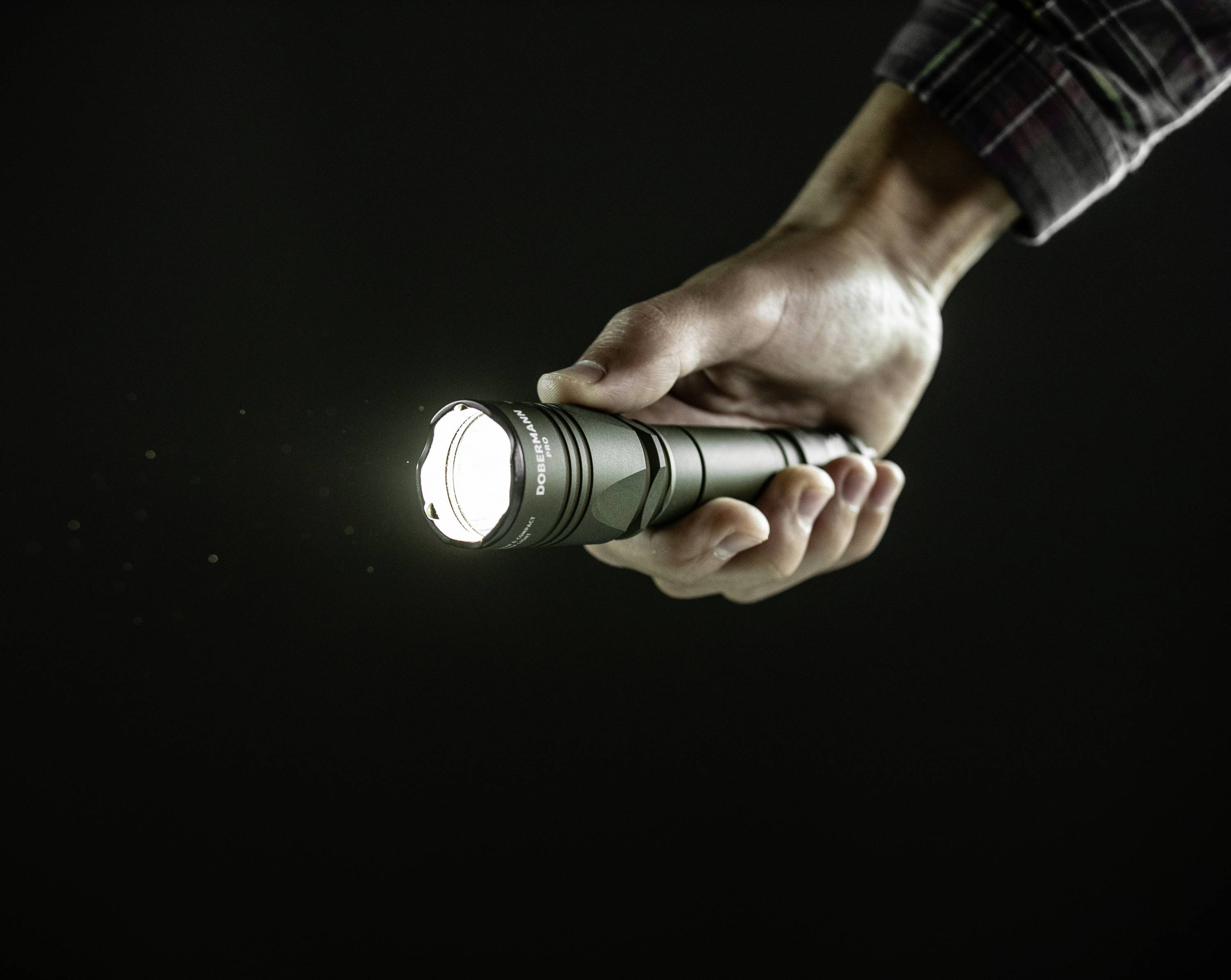 Eine Hand hält eine eingeschaltete Taschenlampe, die in einem dunklen Raum leuchtet.