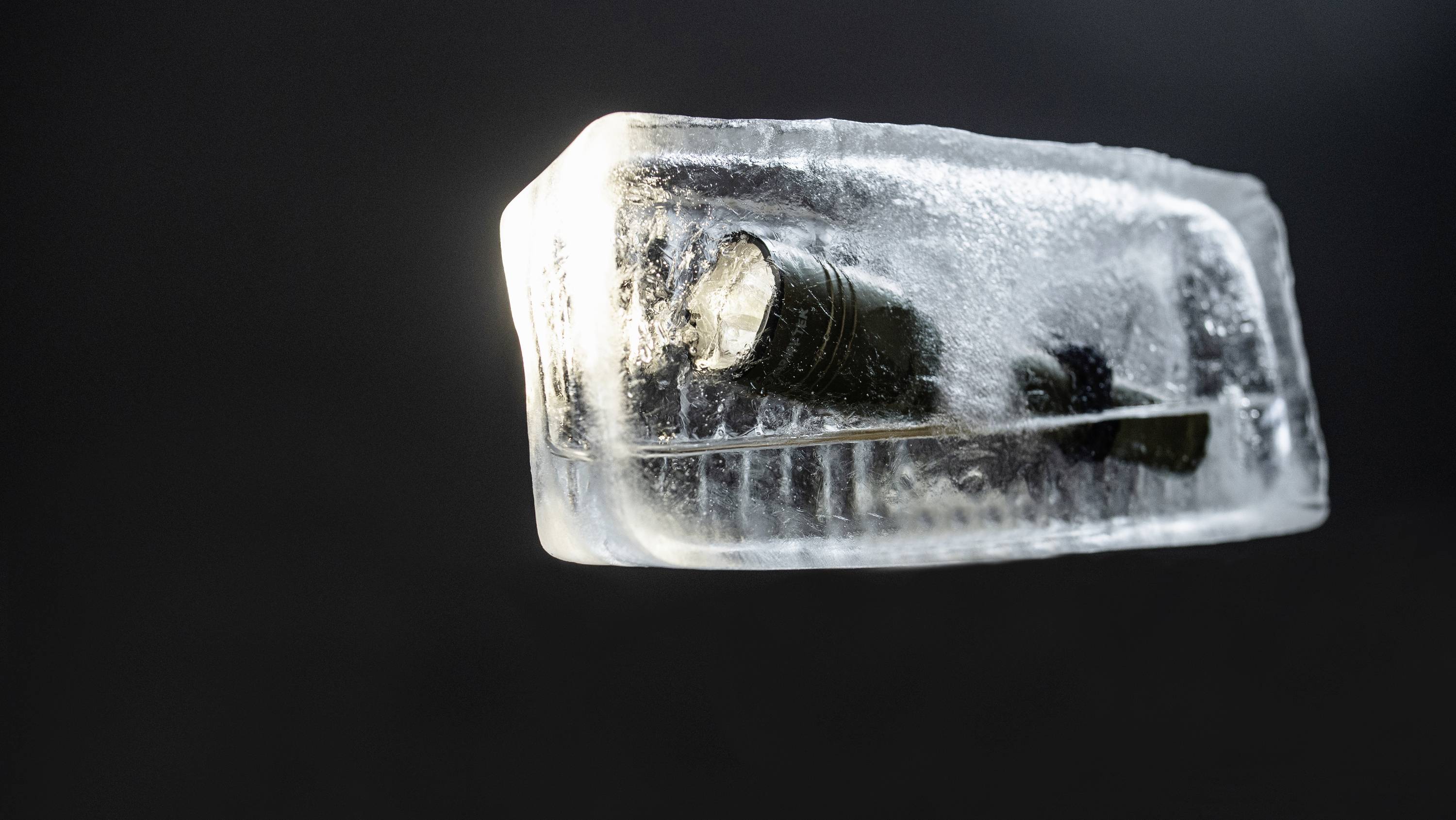 Taschenlampe im Eisblock eingefroren, vor einem dunklen Hintergrund.