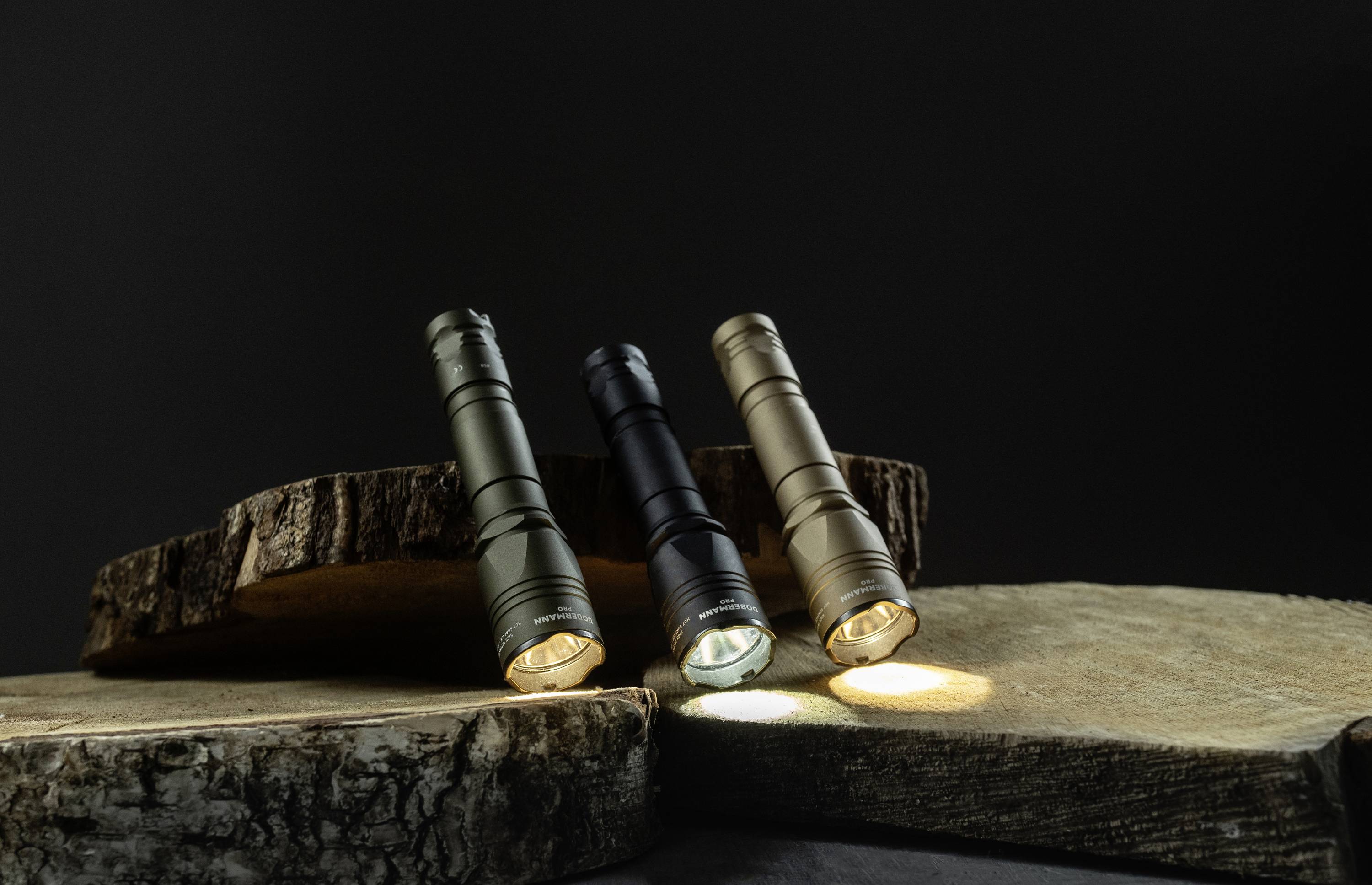 Drei Taschenlampen in verschiedenen Farben stehen auf Holzstücken und leuchten leicht in einem dunklen Hintergrund.
