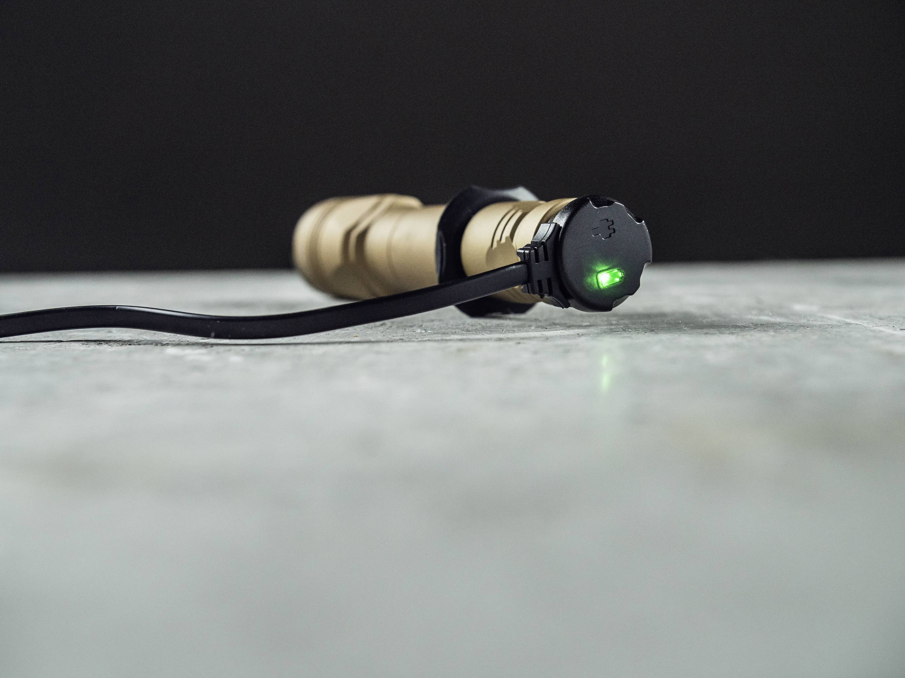 Eine Taschenlampe wird über ein Kabel geladen. Eine grüne LED leuchtet auf dem Ladeanschluss und signalisiert den Ladevorgang.