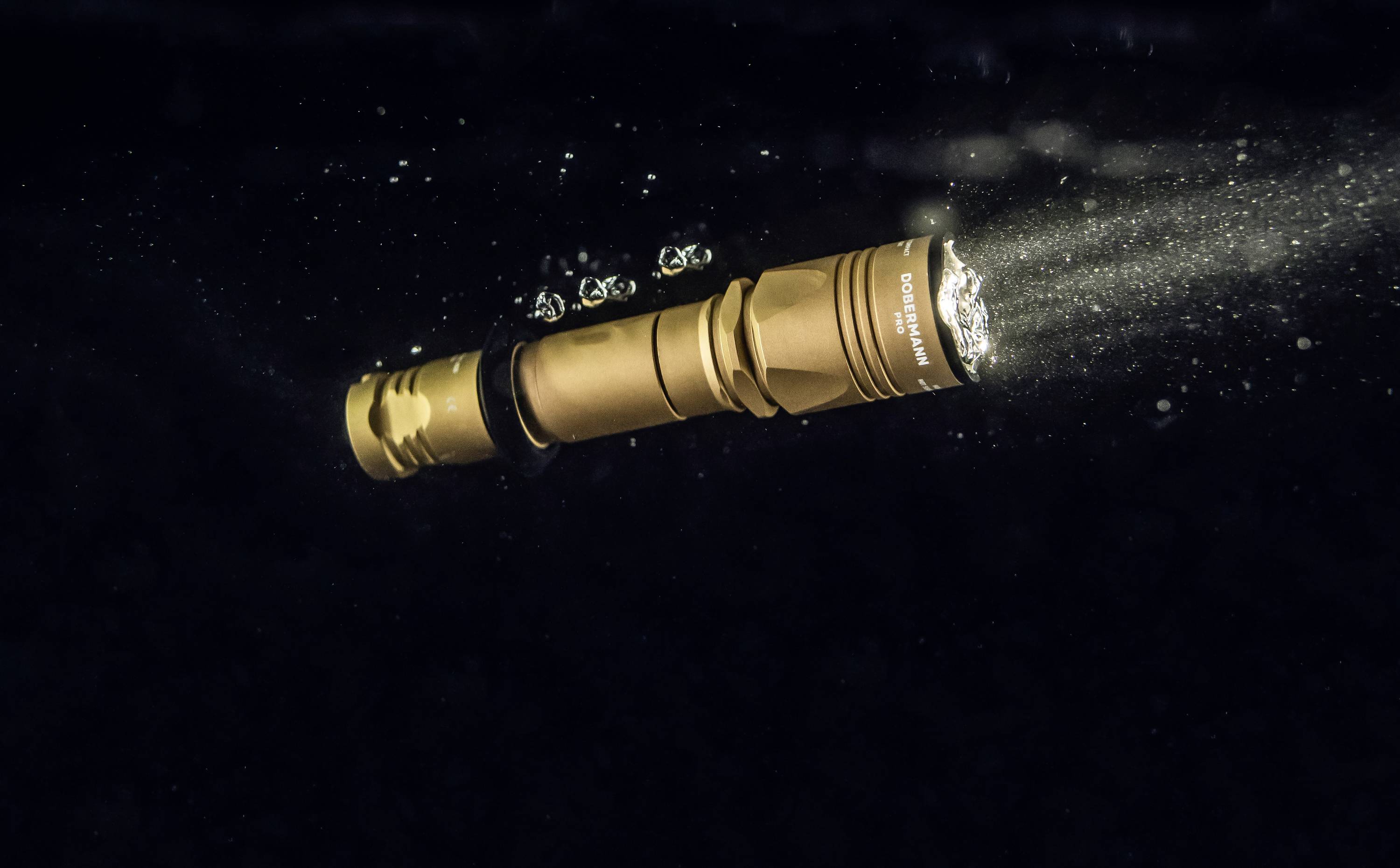 Eine goldene wasserdichte Taschenlampe leuchtet unter Wasser und erzeugt kleine Luftblasen. Sie ist nach rechts oben gerichtet.