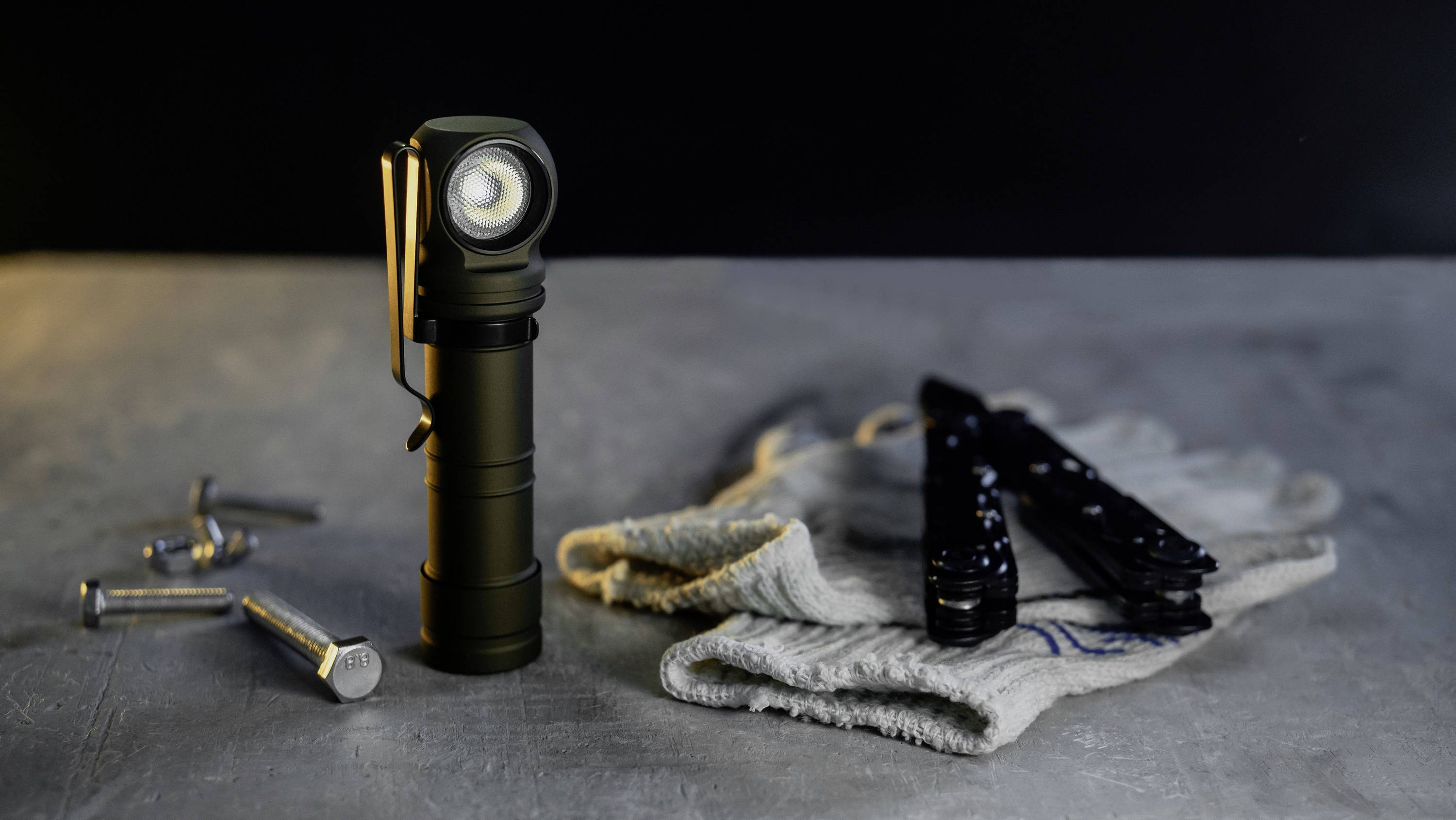 Taschenlampe steht auf einem Tisch neben einem weißen Tuch und mehreren kleinen Schrauben; Werkzeug im Hintergrund.