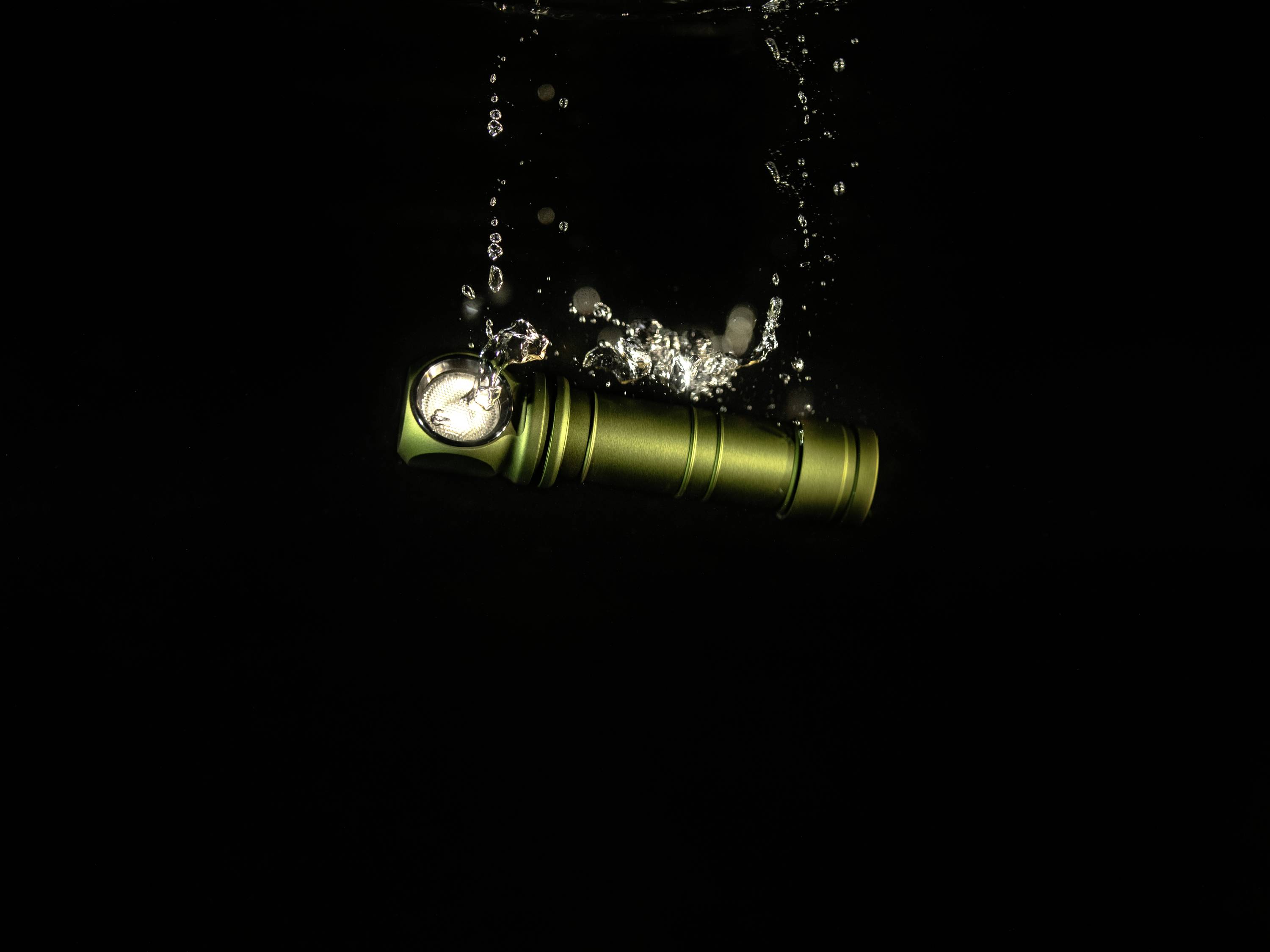 Eine grüne Taschenlampe fällt ins Wasser, Blasen steigen auf. Dunkler Hintergrund hebt die Bewegung und Helligkeit hervor.