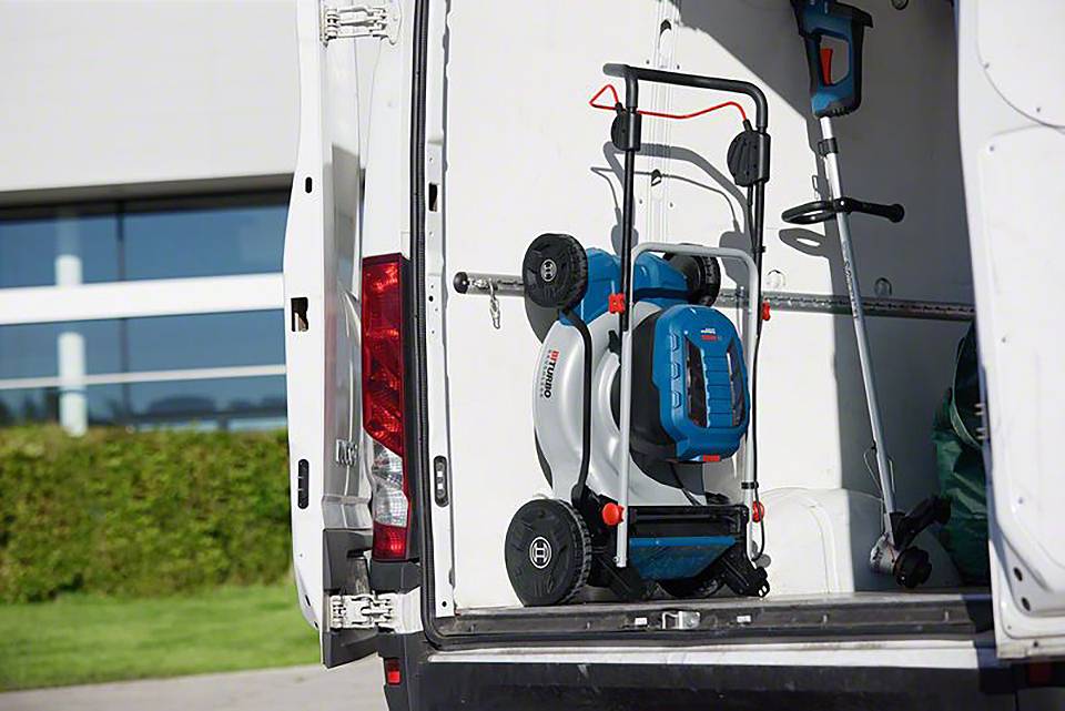 Rasenmäher und Gartengeräte in der Ladefläche eines weißen Transporters, bereit für den Transport oder Einsatz.