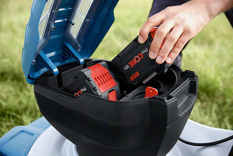 Eine Hand legt einen Akku in ein batteriebetriebenes Gartengerät ein. Der Akku ist schwarz mit roten Akzenten und trägt die Aufschrift 'ProCORE'.