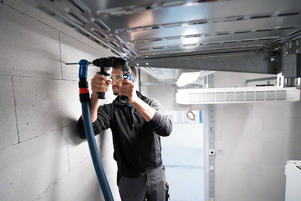 Ein Mann installiert blaue Kabel in einem Technikraum. Er steht auf einer Leiter und arbeitet nah an der Decke.