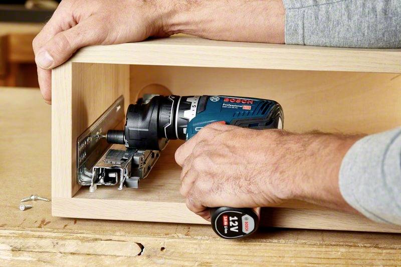 Eine Person montiert ein Metallscharnier in einen Holzkasten mit einem elektrischen Schraubenzieher.