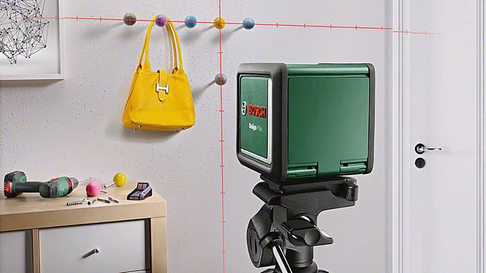 Ein grüner Laser-Wasserwaagenprojektor zeigt horizontale und vertikale Linien an der Wand neben einer gelben Handtasche.