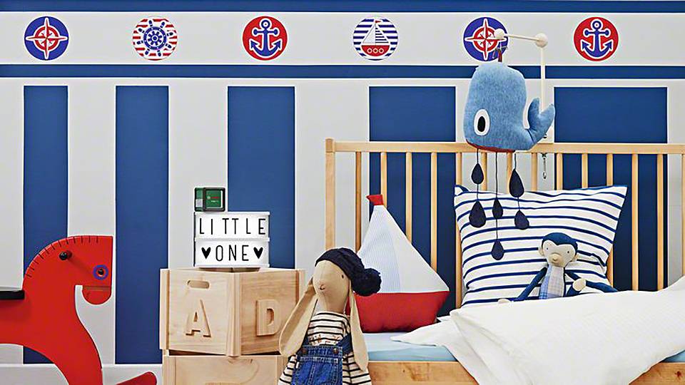 Ein Kinderzimmer mit maritimen Thema. Ein Kinderbett ist von Spielzeug und Dekorationen umgeben, darunter ein rotes Schaukelpferd.