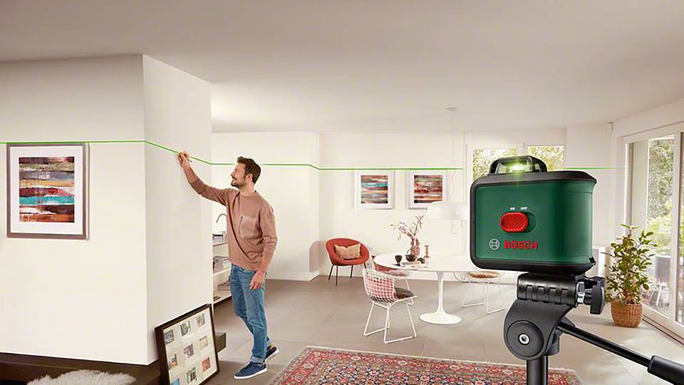 Mann richtet mithilfe eines Bosch-Lasergeräts eine grüne Linie an der Wand einer modern eingerichteten Wohnung aus.