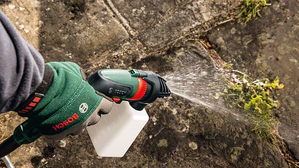 Eine Person sprüht eine Flüssigkeit mit einem Hochdruckreiniger auf vermooste Pflastersteine, um sie zu reinigen.