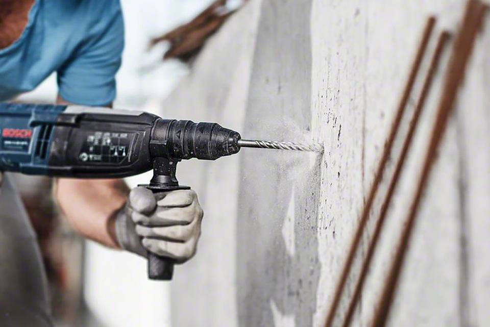 Eine Person bohrt ein Loch in eine Betonwand mit einer elektrischen Bohrmaschine, während sie Arbeitshandschuhe trägt.