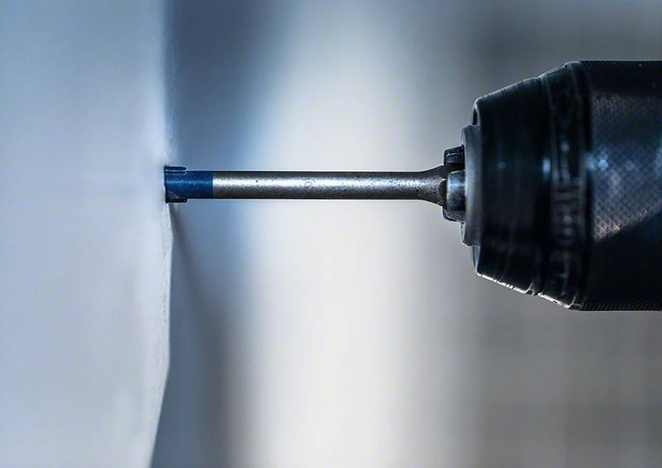 Nahaufnahme eines elektrischen Bohrers, der in eine weiße Wand bohrt.