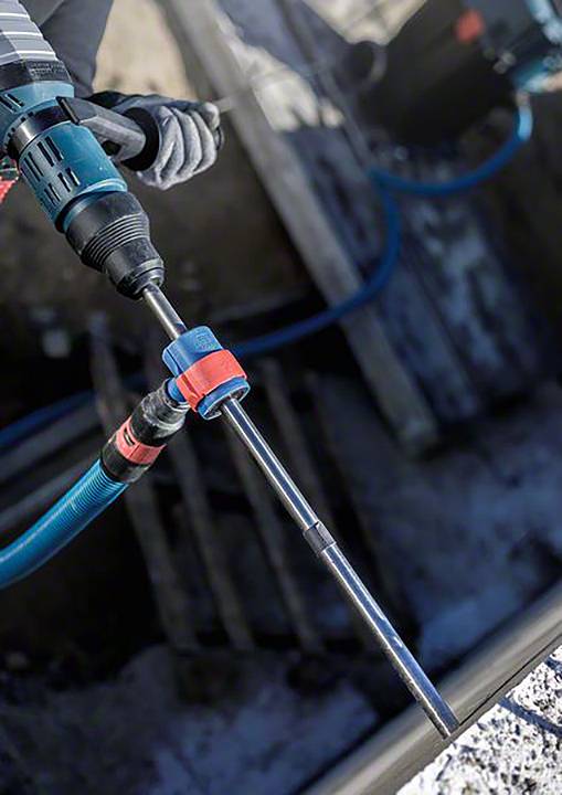 Eine Person arbeitet mit einem elektrischen Bohrhammer auf einer Baustelle. Der Bohrer ist in Metall eingerastet.