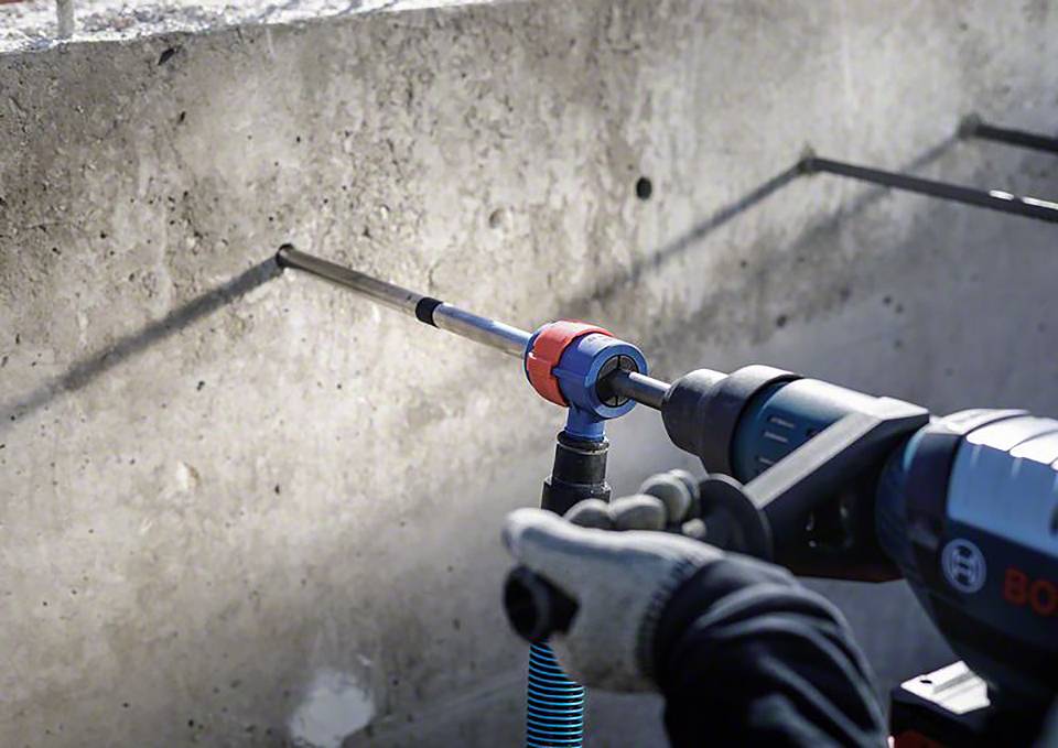 Eine Person bohrt mit einer elektrischen Bohrmaschine Löcher in eine Betonwand. Schutzkleidung an den Händen ist sichtbar.