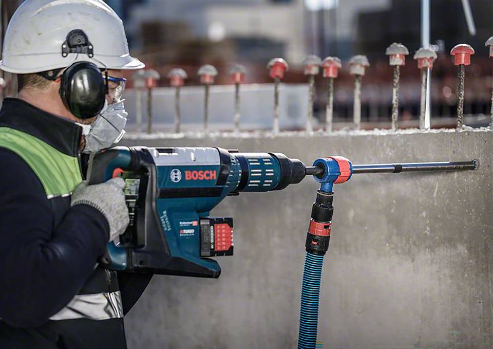 Ein Arbeiter in Schutzkleidung bohrt mit einem Bosch-Bohrhammer in eine Betonwand, umgeben von Bewehrungsstangen.