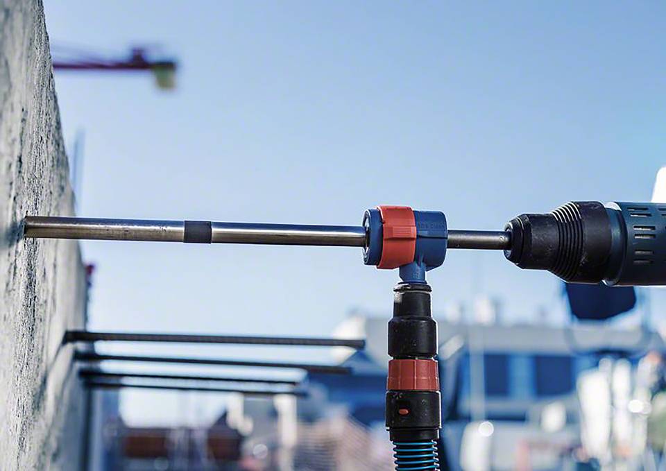 Elektrowerkzeug bohrt ein Loch in eine Betonwand, im Hintergrund verschwommen eine Baustelle mit Kran.