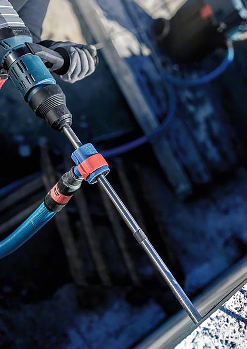 Eine Person benutzt eine elektrische Bohrmaschine auf einer Baustelle. Die Bohrspitze ist in ein festes Material eingetaucht.