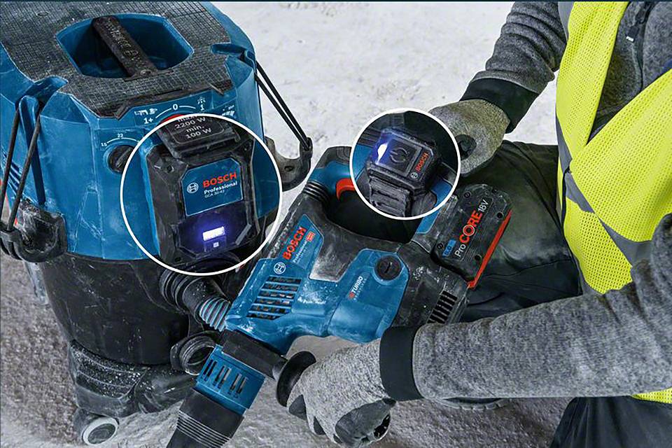 Eine Person benutzt ein elektrisches Bosch-Werkzeug mit einem entsprechenden Akku, während ein Staubsauger daneben steht.