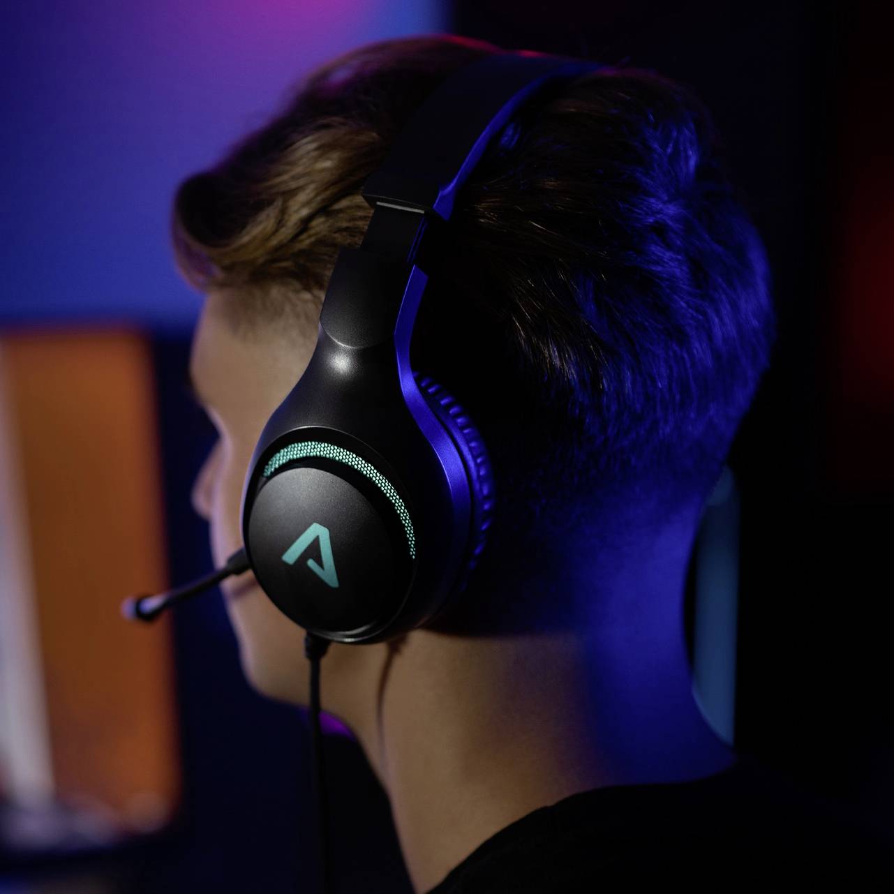 Eine Person trägt ein Gaming-Headset mit Mikrofon in einem schwach beleuchteten Raum. Das Logo auf dem Kopfhörer leuchtet blau.