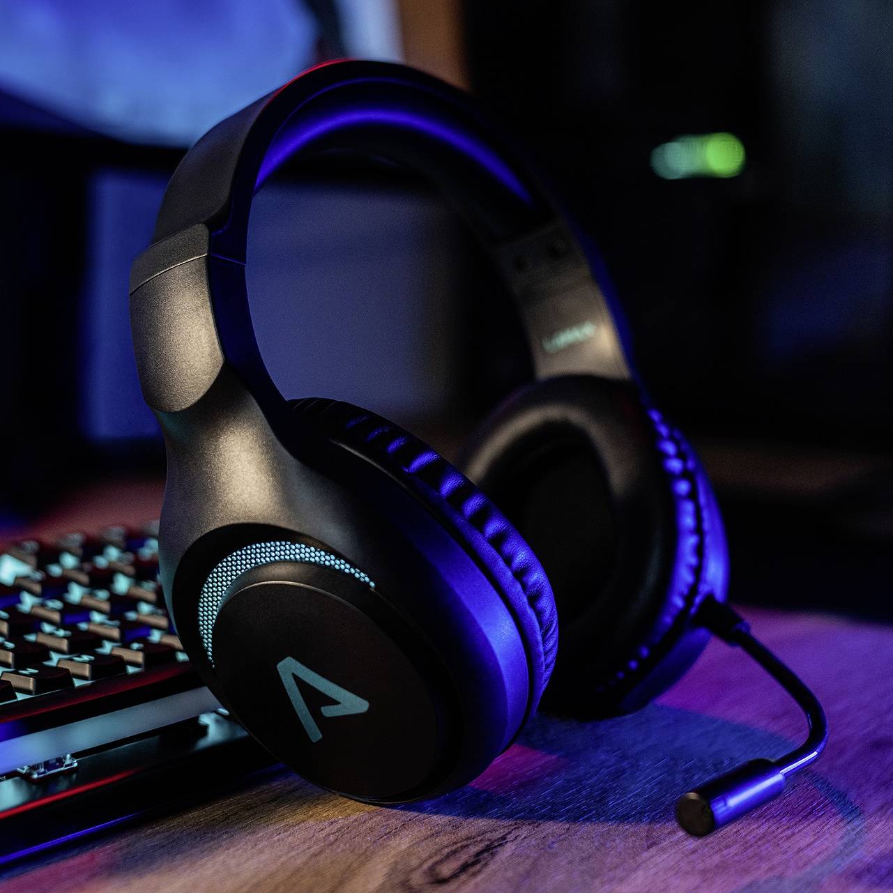 Ein Gaming-Headset liegt auf einem Schreibtisch neben einer beleuchteten Tastatur. Die Szene ist in blauem Licht gehalten.