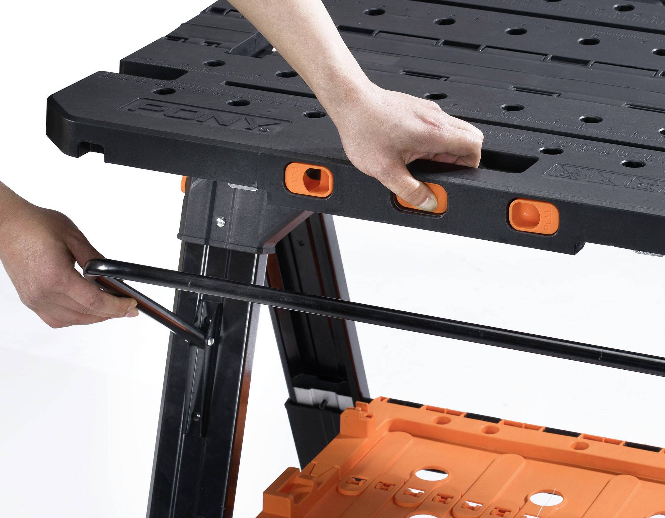 Person montiert einen schwarzen Klapptisch mit orangen Knöpfen, indem sie eine Metallstange in die Tischbeine einsetzt.