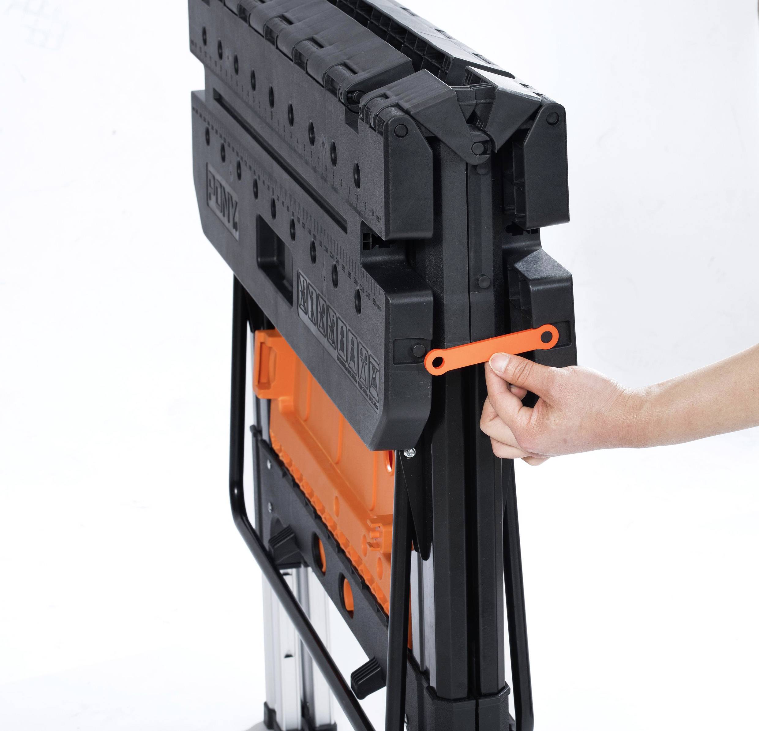 Person klappt einen schwarzen zusammenklappbaren Werktisch mit orangefarbenen Details zusammen.
