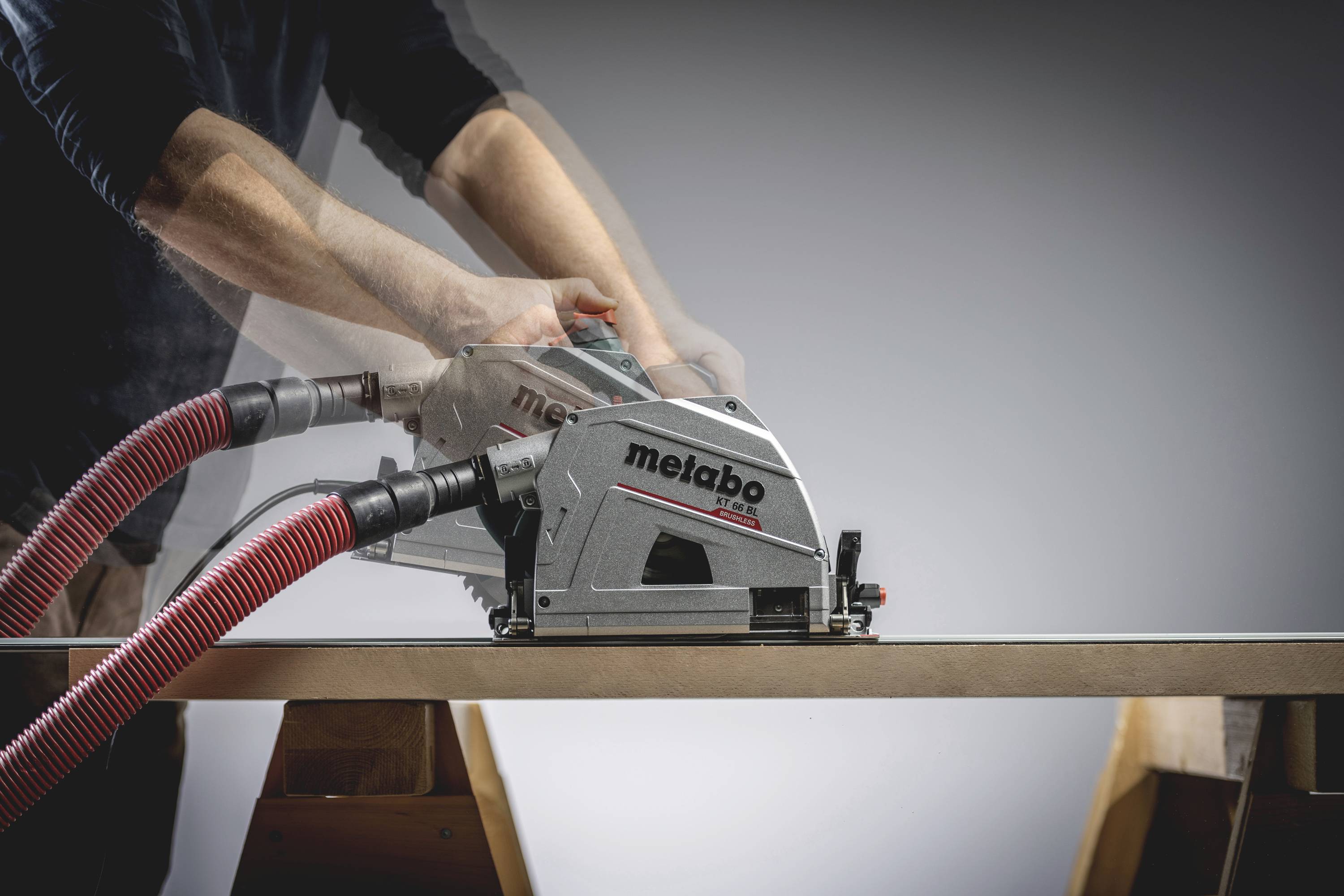 Eine Person verwendet eine Metabo-Kreissäge, um ein Holzbrett zu schneiden. Rotes Staubsaugerrohr ist an der Säge angeschlossen.
