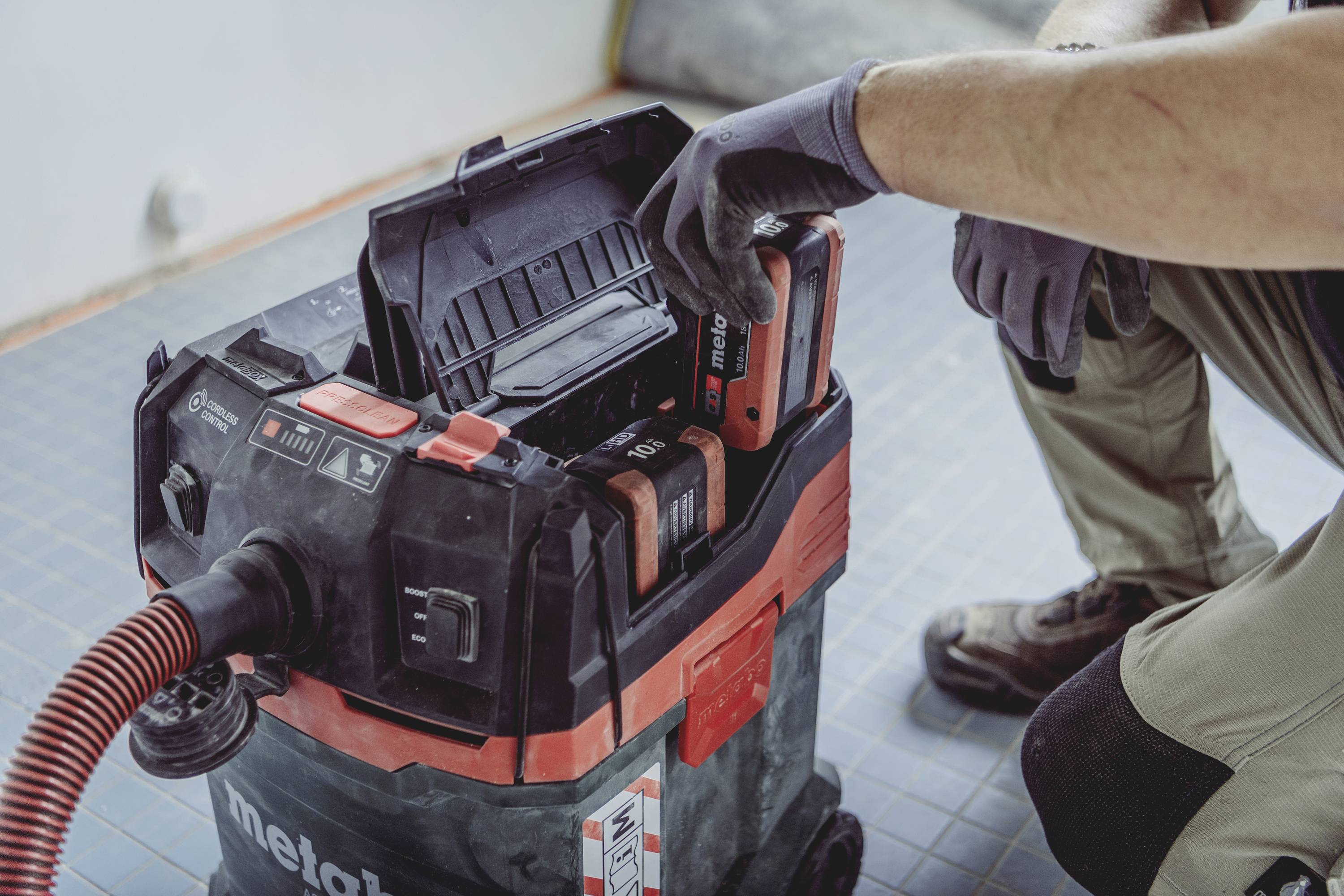 Eine Person setzt einen Staubsauger-Akku in einen industriellen Werkstattsauger ein, bereit für den Einsatz auf einer Baustelle.