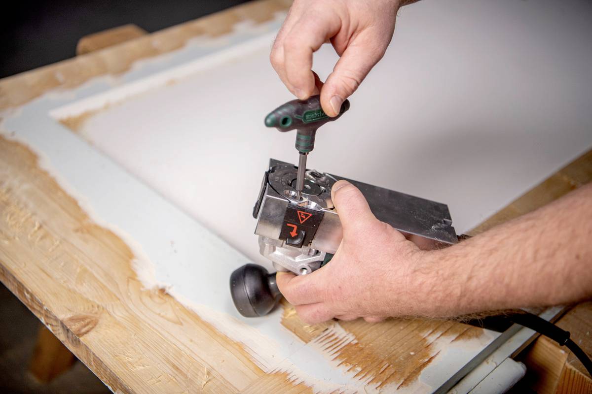 Eine Person arbeitet mit einem Holzbearbeitungswerkzeug, um einen Rahmen auf einem Holztisch zu bearbeiten.