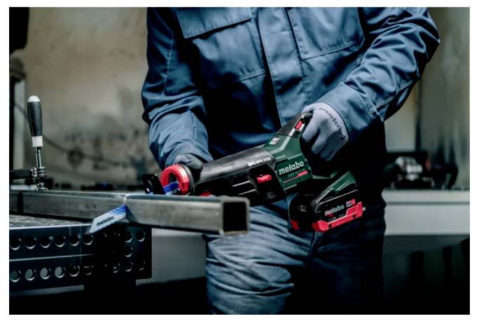 Eine Person in Schutzkleidung bedient eine Kreissäge und schneidet in einer Werkstatt einen Metallträger, wobei Präzision und Sicherheit betont werden.