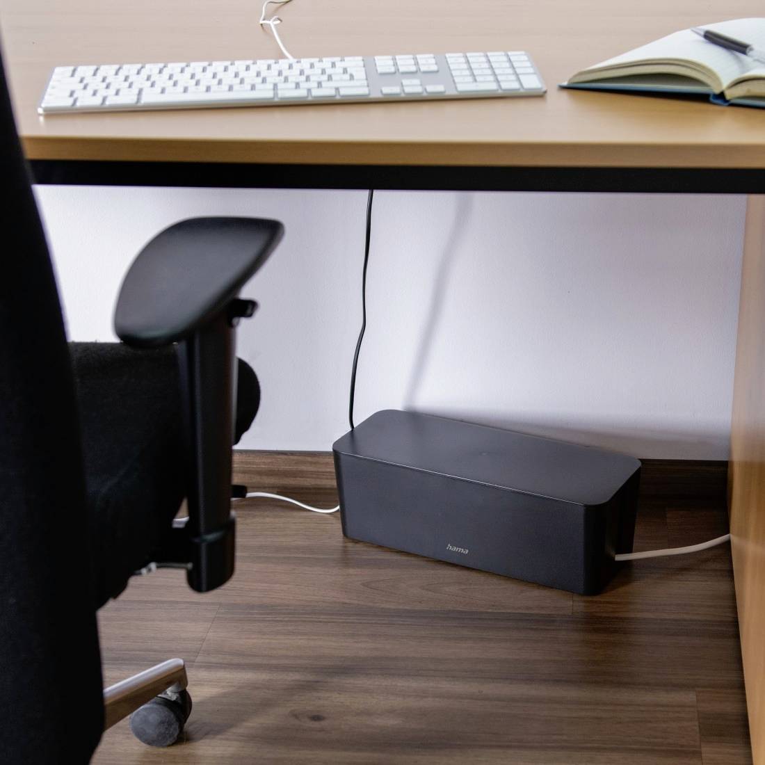 Ein Schreibtisch mit Tastatur, Buch und Stuhl. Unter dem Tisch befindet sich ein Kabelmanagement-System, das Kabel ordnet.