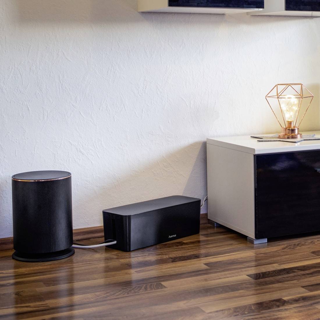 Ein moderner Wohnzimmerbereich mit Holzboden, einem schwarzen Möbelstück, auf dem eine geometrische Lampe steht, und einem Wi-Fi-Gerät.