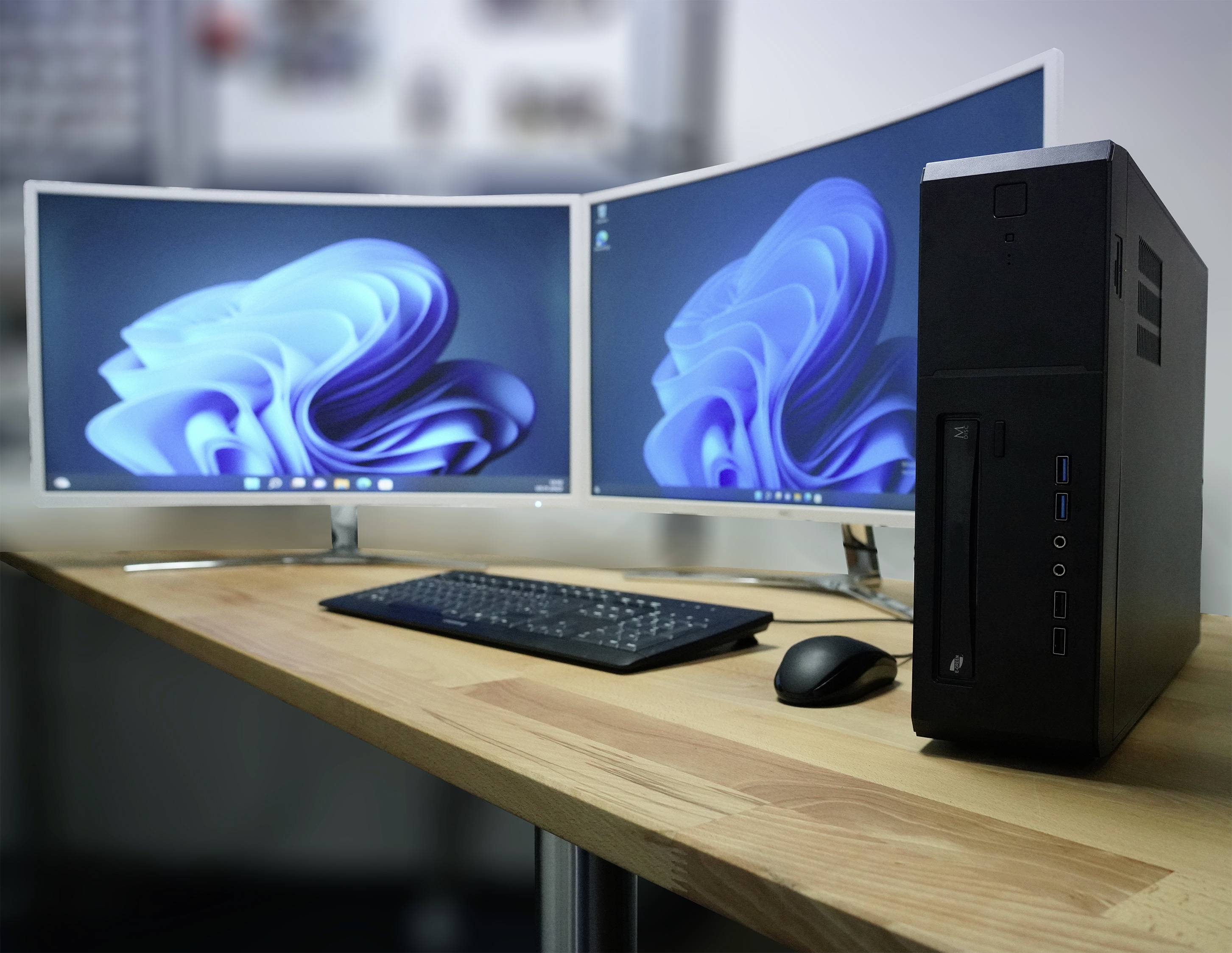 Ein Schreibtisch mit zwei gebogenen Monitoren, einem Computergehäuse, einer Tastatur und einer Maus in einem modernen Büro.