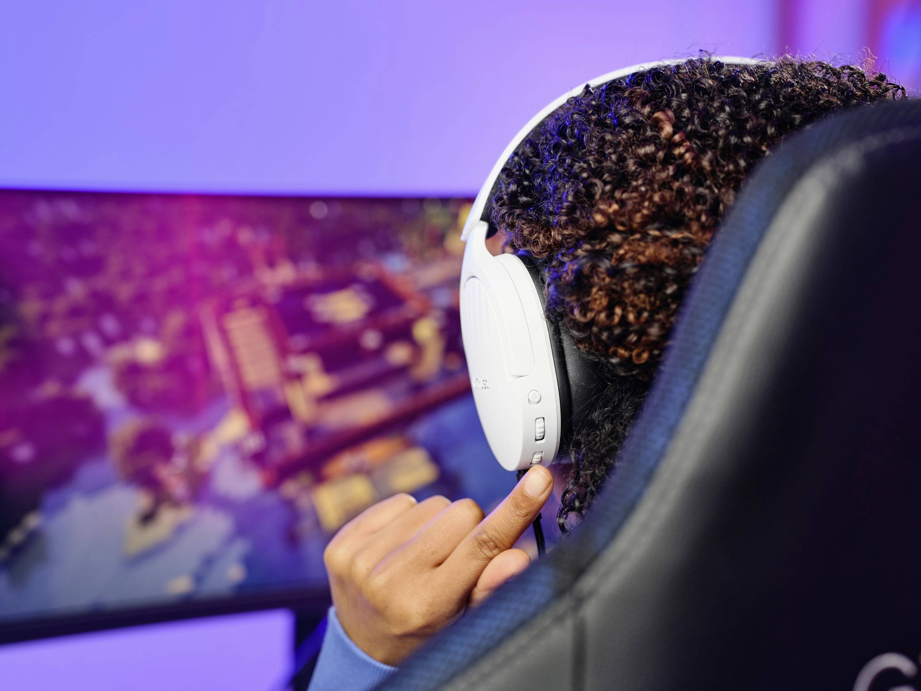 Eine Person mit weißen Kopfhörern spielt ein Videospiel auf einem Flachbildschirm. Das Bild hat einen Fokus auf das Gaming-Erlebnis.