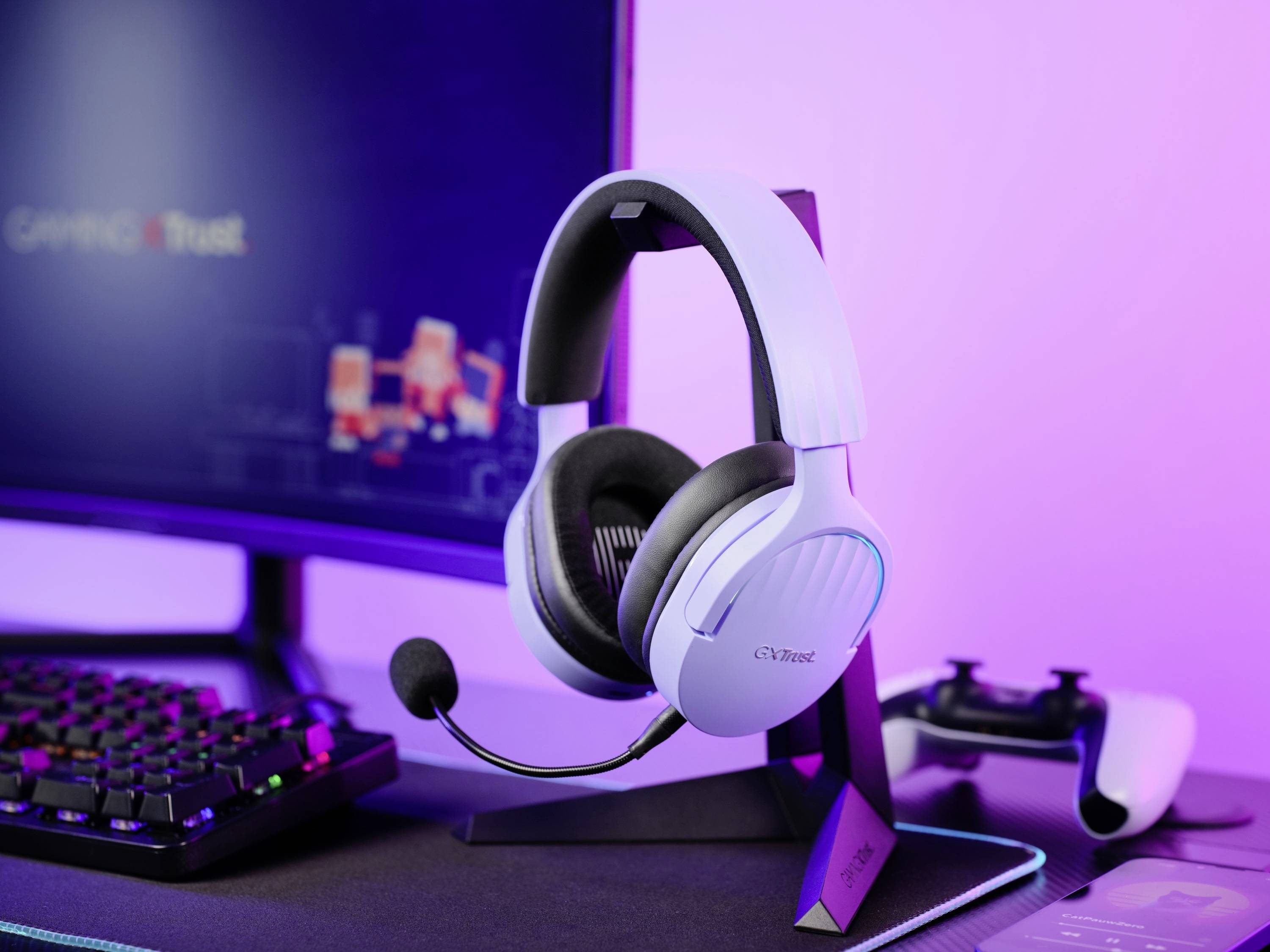 Ein Gaming-Headset steht auf einem Schreibtisch neben einer Tastatur und einem Bildschirm. Im Hintergrund ist ein Game-Controller zu sehen.
