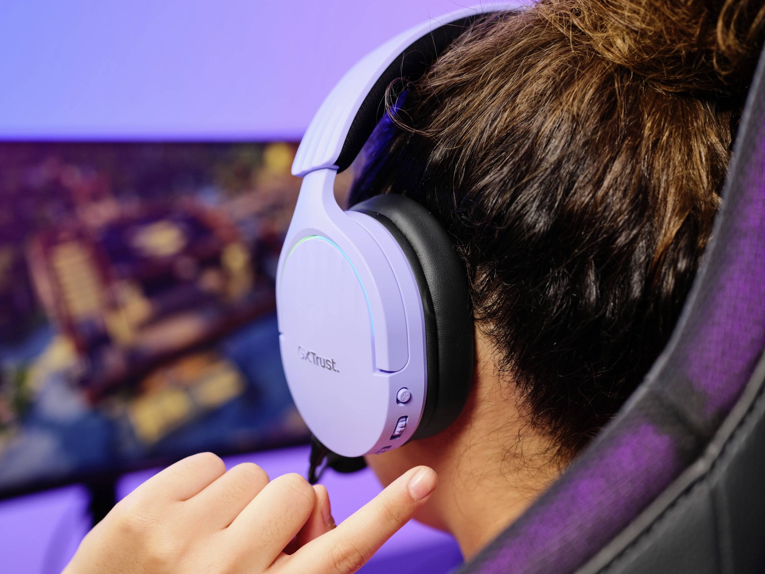 Eine Person trägt ein weißes Headset und sitzt vor einem Monitor. Sie berührt die Lautstärkesteuerung am Headset, während ein Spiel auf dem Bildschirm läuft.