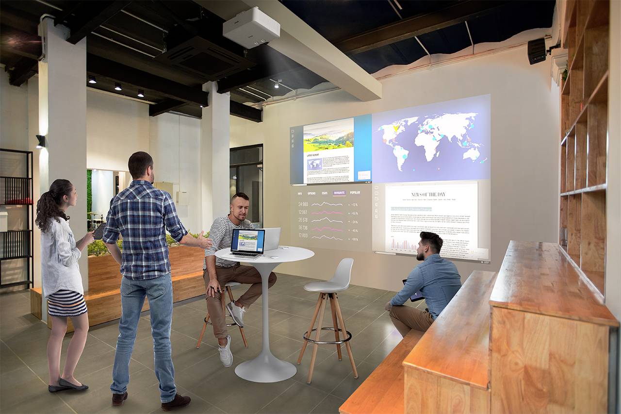 Eine Gruppe von Personen diskutiert in einem modernen Büro, während auf einer Wand Karte und Diagramme projiziert werden.