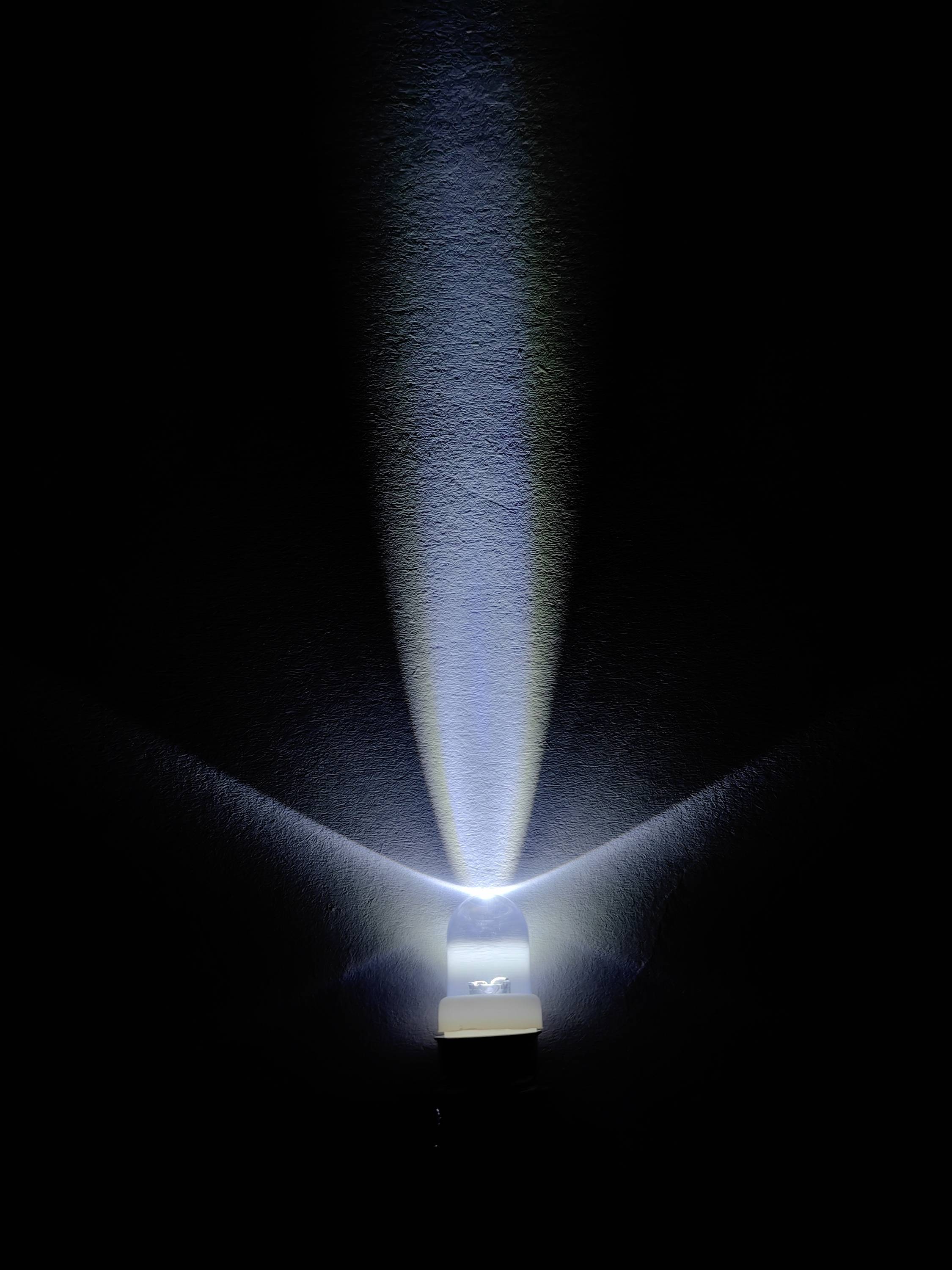 Ein Lichtstrahl aus einem kleinen Gerät projiziert fächerförmig auf eine Wand, erzeugt ein symmetrisches, leuchtendes Muster.