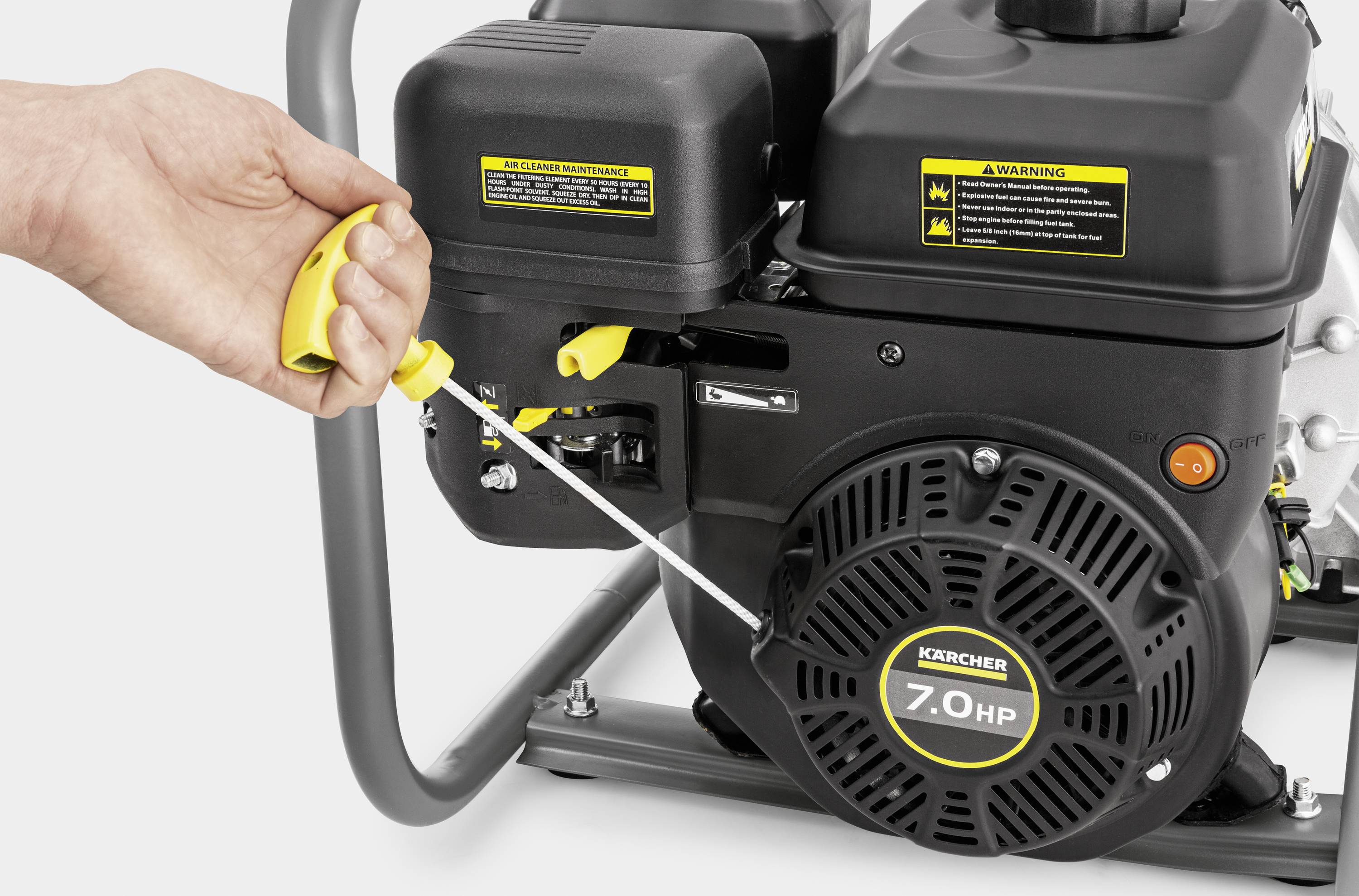 Eine Hand zieht die Startleine eines 7,0 HP Motors einer Reinigungsmaschine. Der Motor trägt Warnhinweise auf den Gehäusen.