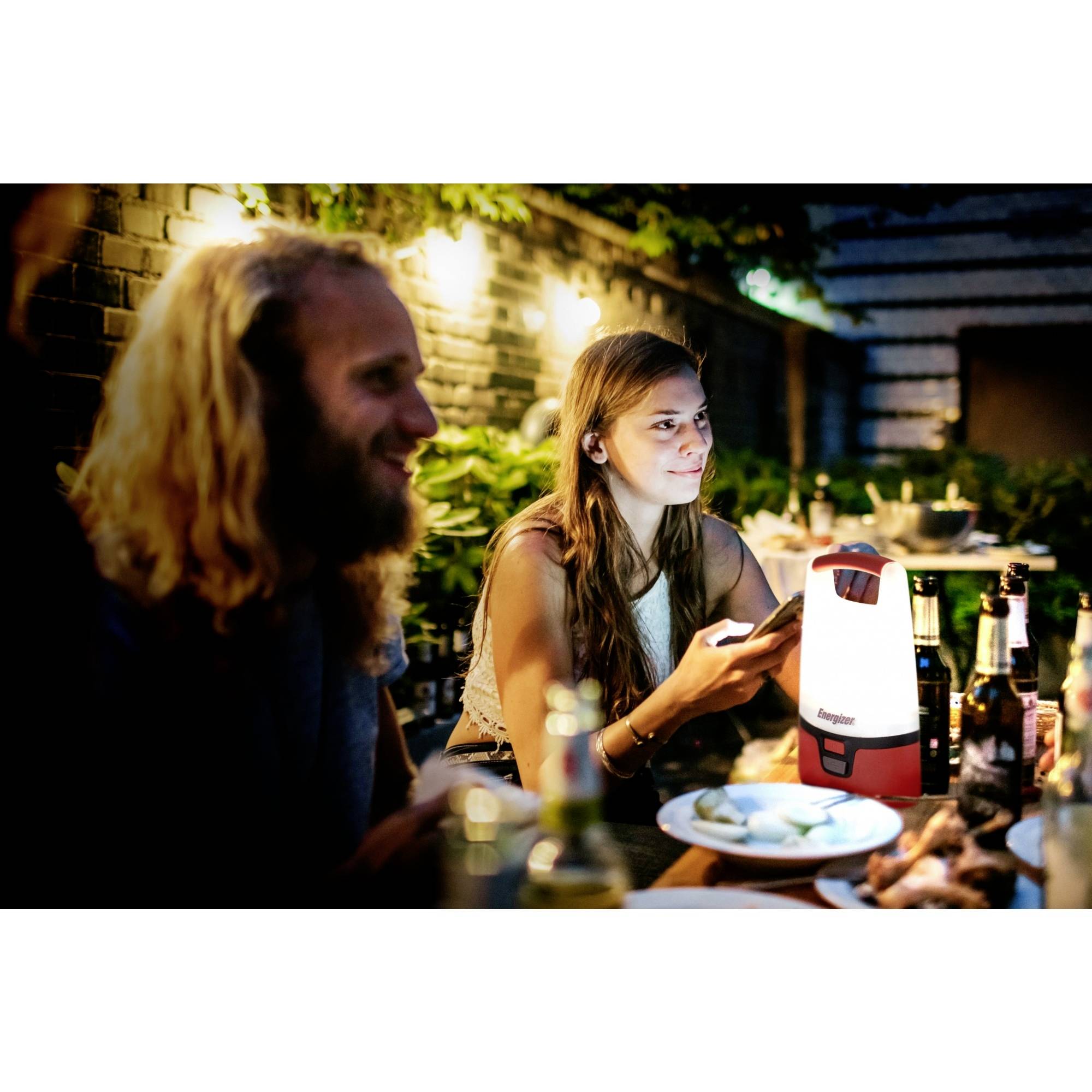 Eine Gruppe von Menschen sitzt bei einem Abendessen im Freien. Auf dem Tisch steht eine leuchtende Lampe. Es herrscht entspannte Stimmung.