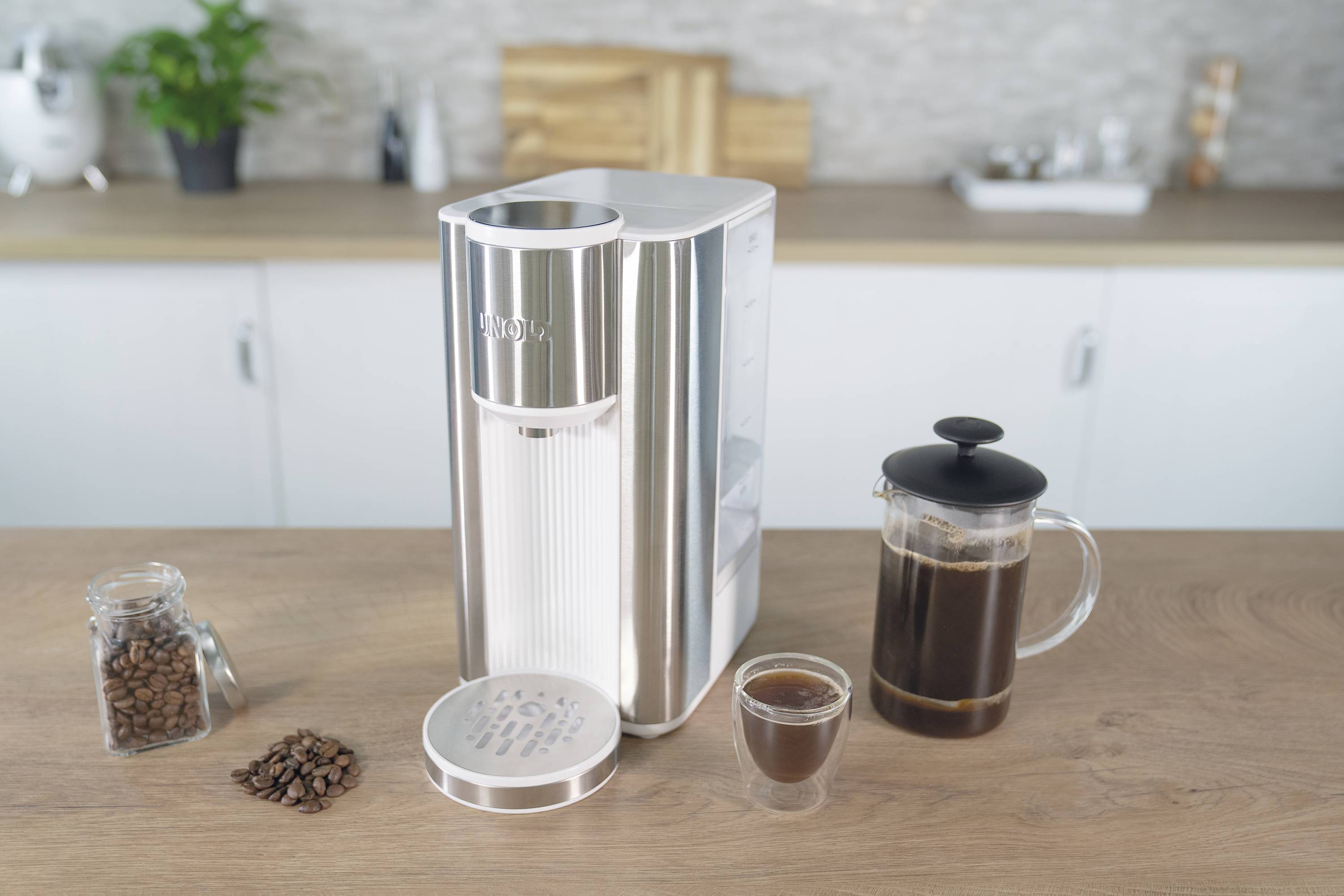 Kaffeemaschine auf einer Küchenarbeitsplatte mit Glas Kaffee, Kaffeebohnen und einer Kaffeepresse daneben.