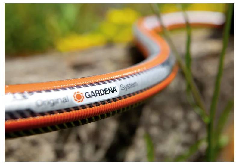 Nahaufnahme eines orange-grauen GARDENA-Gartenschlauchs, der über eine felsige Außenfläche liegt, mit unscharfem Grün im Hintergrund.
