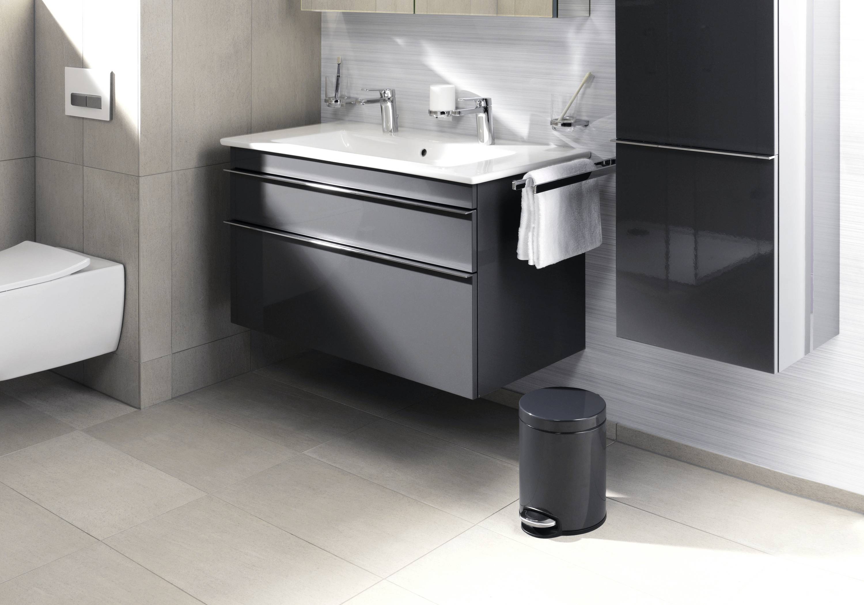 Ein modernes Badezimmer mit einem schwarzen Unterschrank unter einem Doppelwaschbecken, Wandtoilette links, Mülleimer rechts.