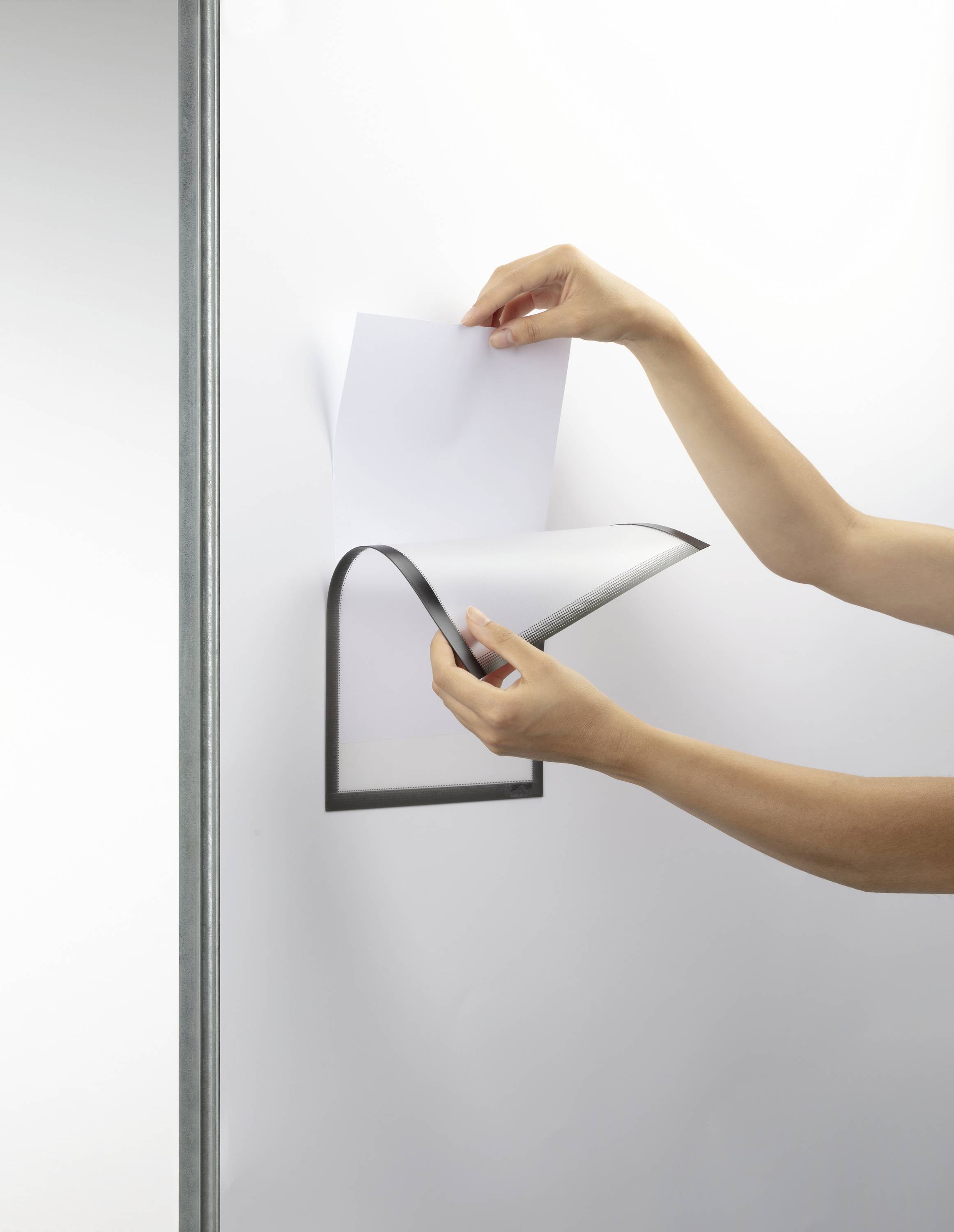 Eine Person blättert an einem Wandhalter für Papierblätter. Der Halter hat ein minimalistisches, modernes Design in Schwarz.
