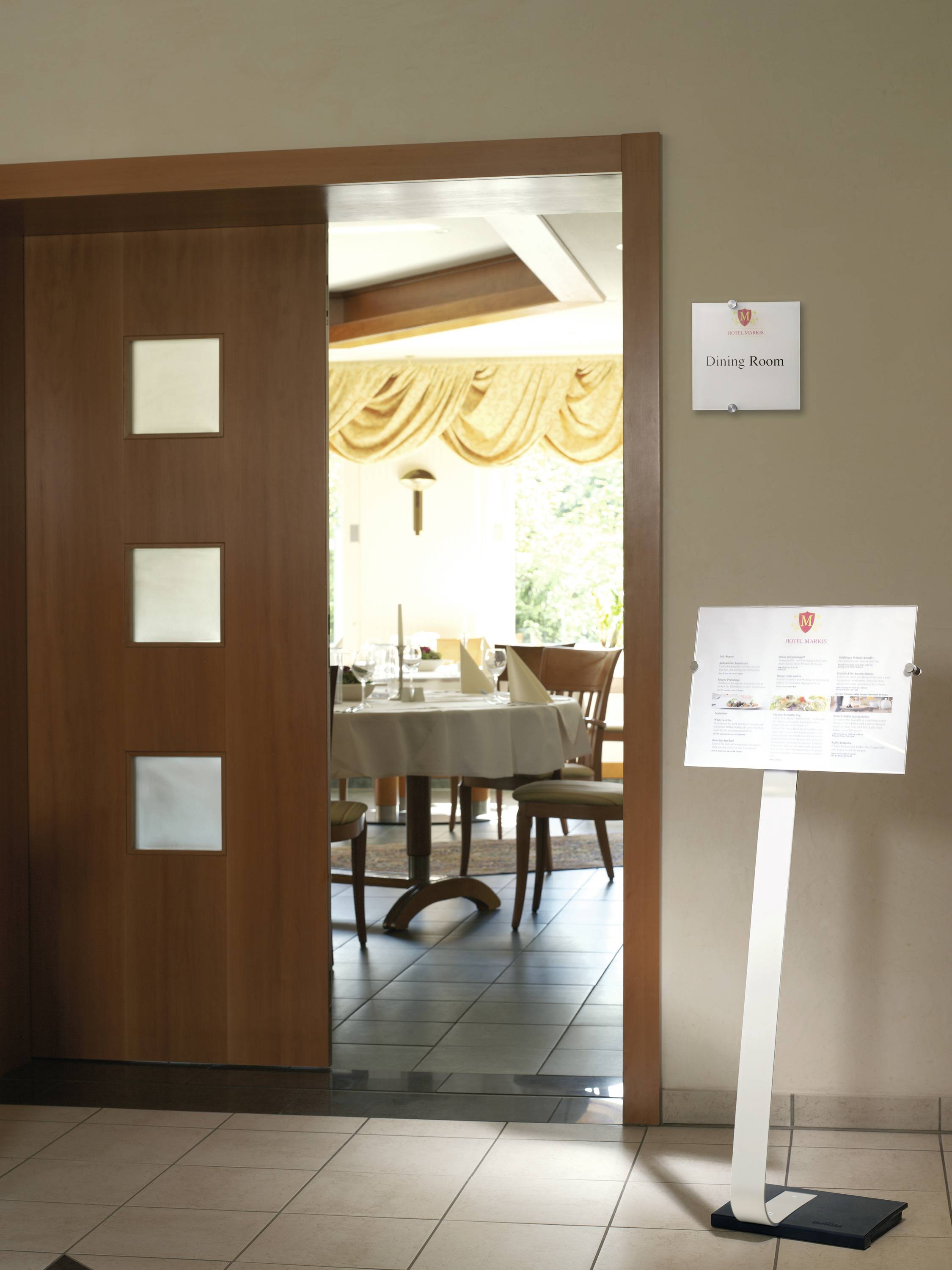 Eingang zu einem Speisesaal mit offenem Holzschiebetor und einem Lesepult. Sicht auf gedeckte Tische im Inneren. Schild: 'Dining Room'.